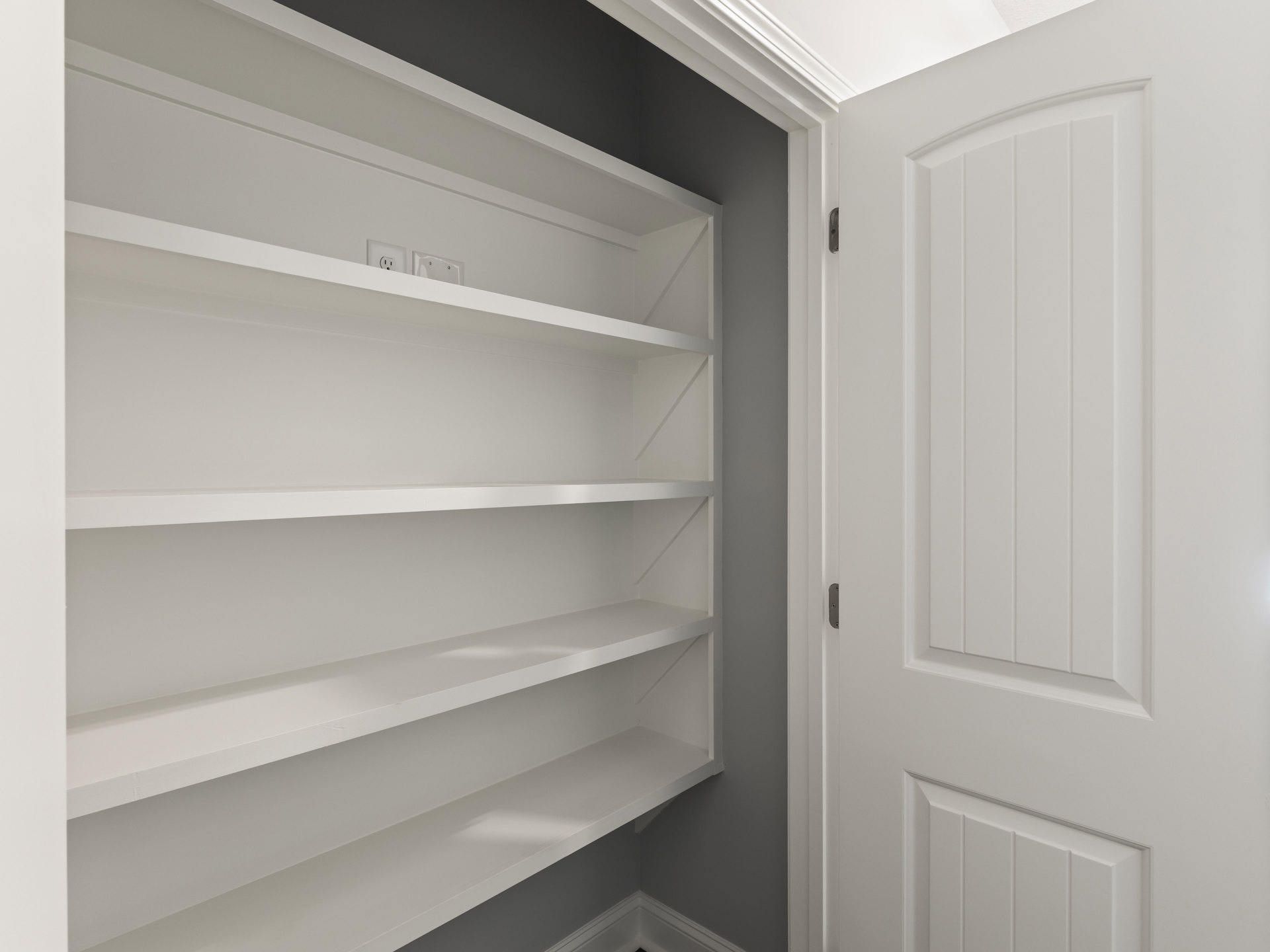 White built-in shelving unit with multiple shelves, integrated power outlet, and silver cabinet handle against a white wall in a modern interior room.