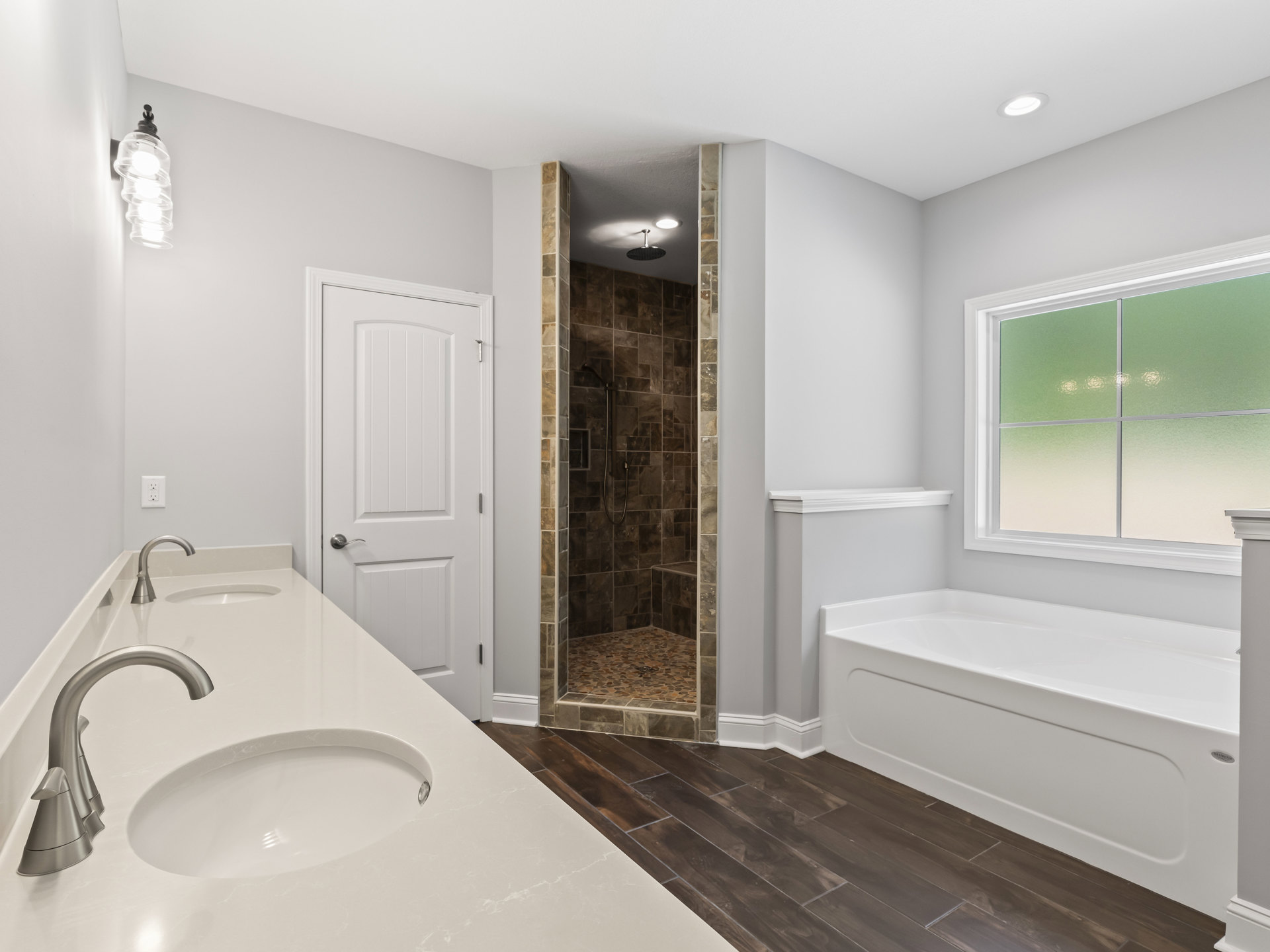 Bathroom with white bathtub, tiled shower, white sink, frosted glass window, silver faucet, white toilet, and white door with silver handle.