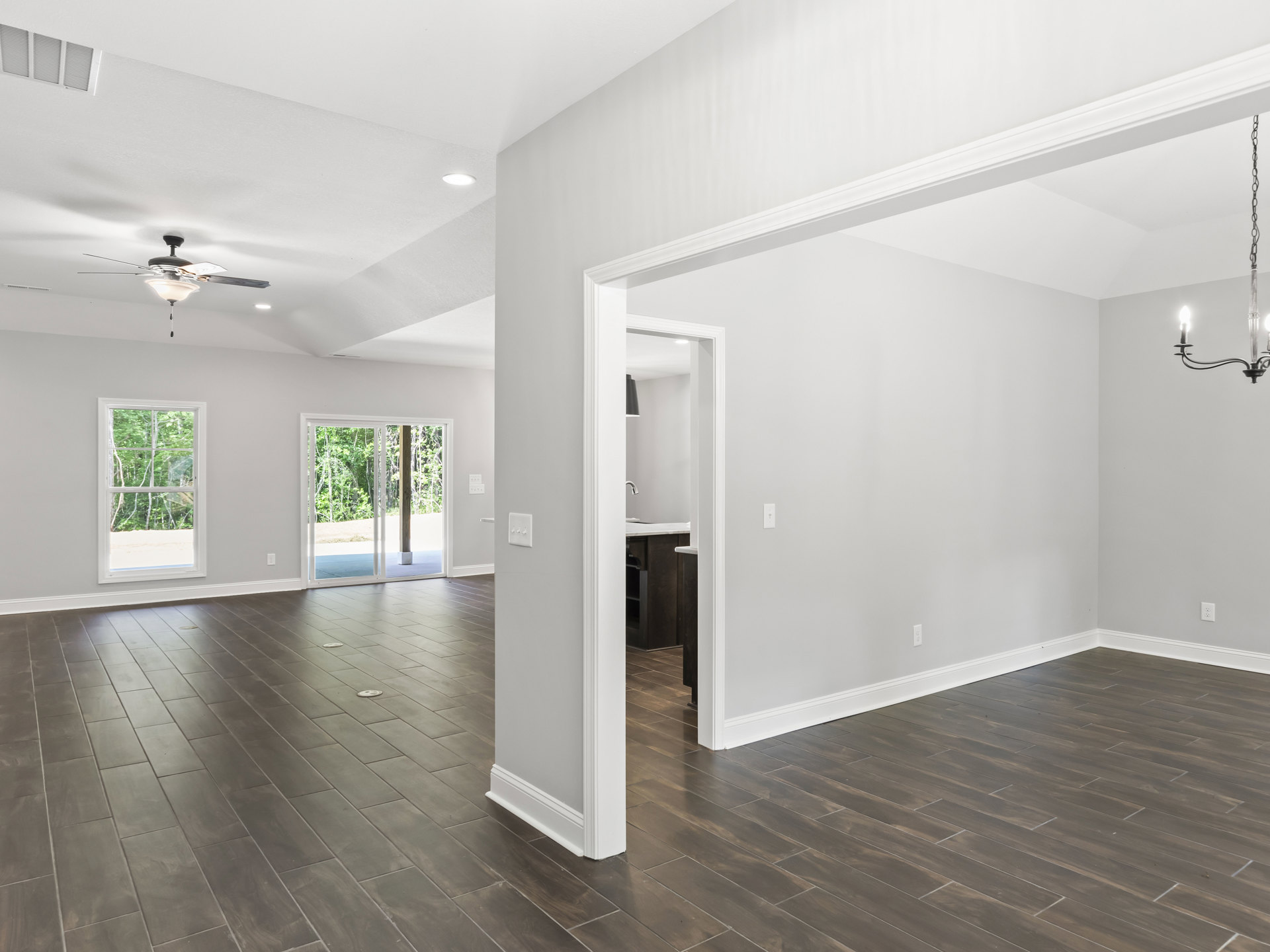 Open living space with wood flooring, white column, ceiling fan with light, large window and sliding glass door overlooking trees