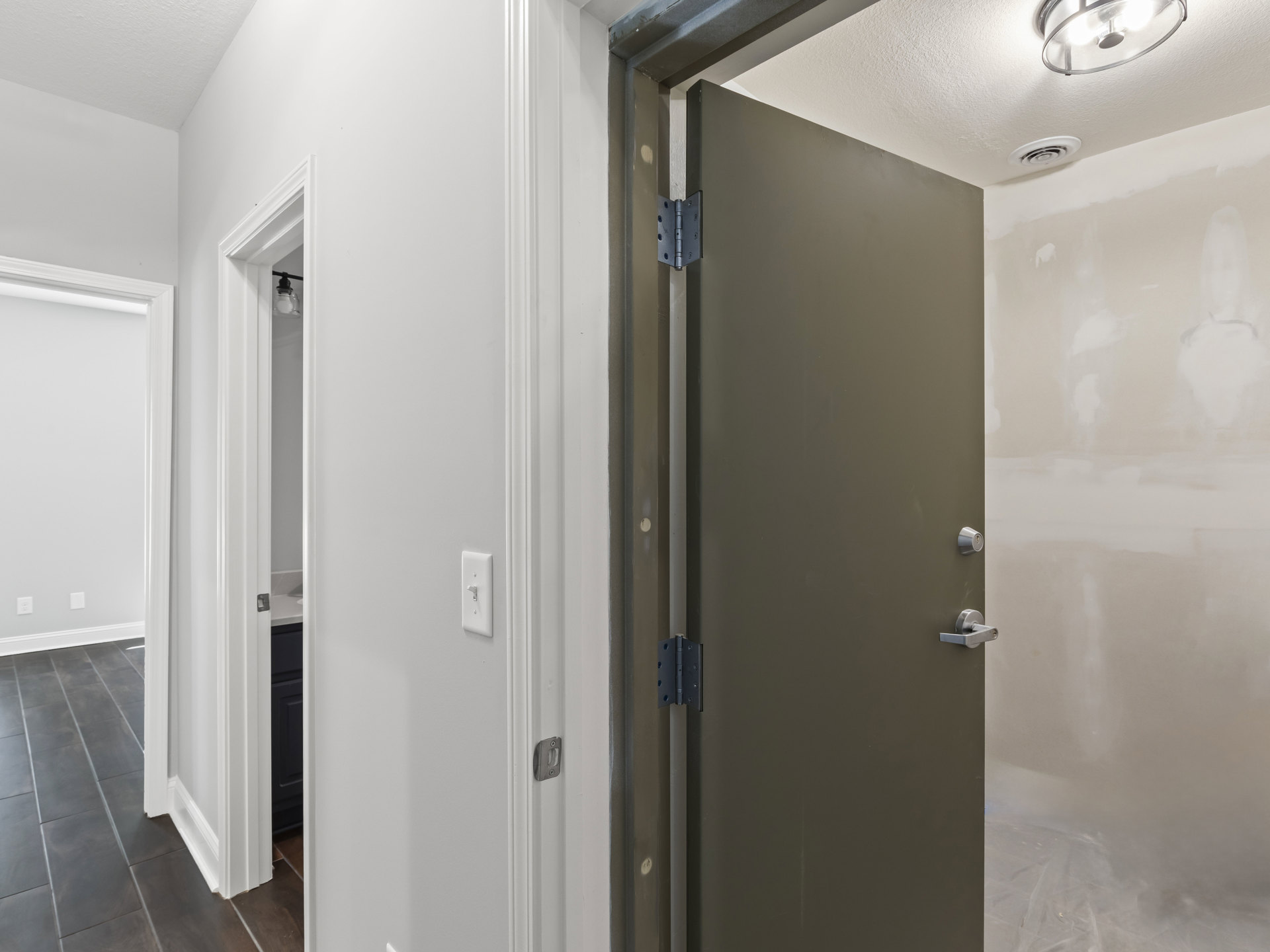 White paneled door with brushed metal handle set in a smooth white wall, dark wood flooring, and modern ceiling light fixture