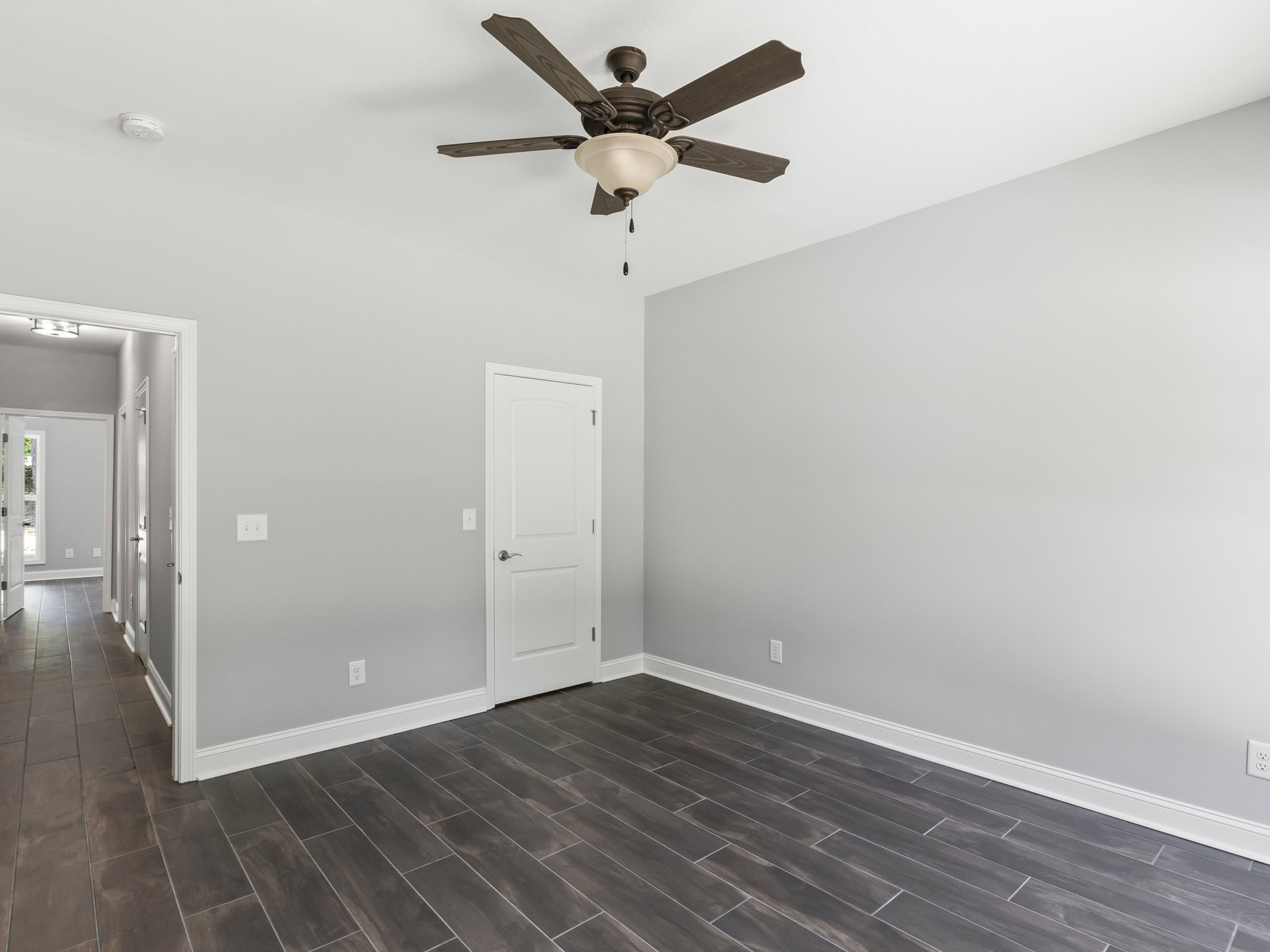 Ceiling fan with integrated light fixture mounted above wood flooring and white trim, white door with silver handle, hallway featuring gray tile floor and white doors
