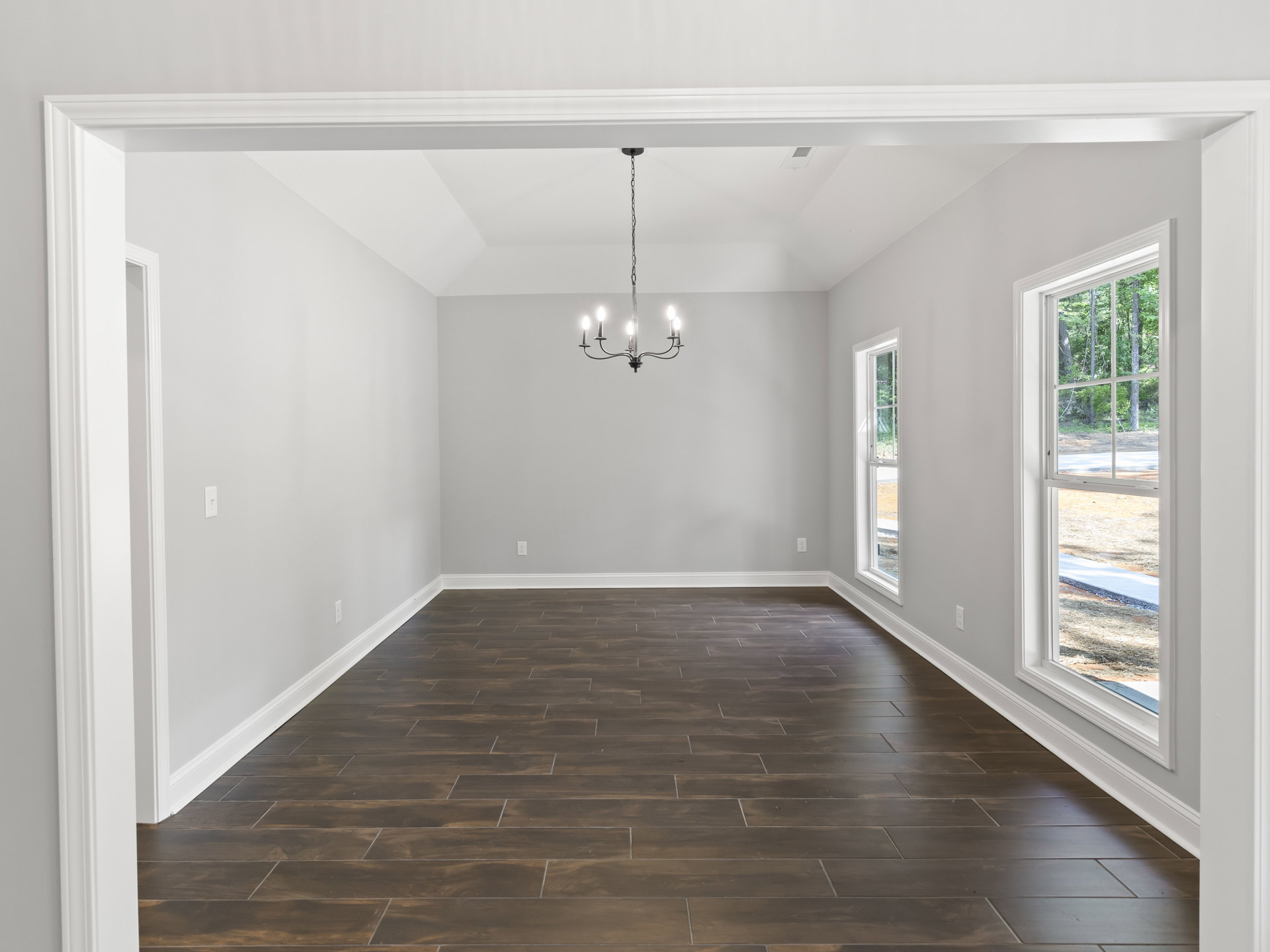 Chandelier with crystal accents hanging from ceiling in a room with white plaster walls, wide wood flooring, and large windows overlooking green trees