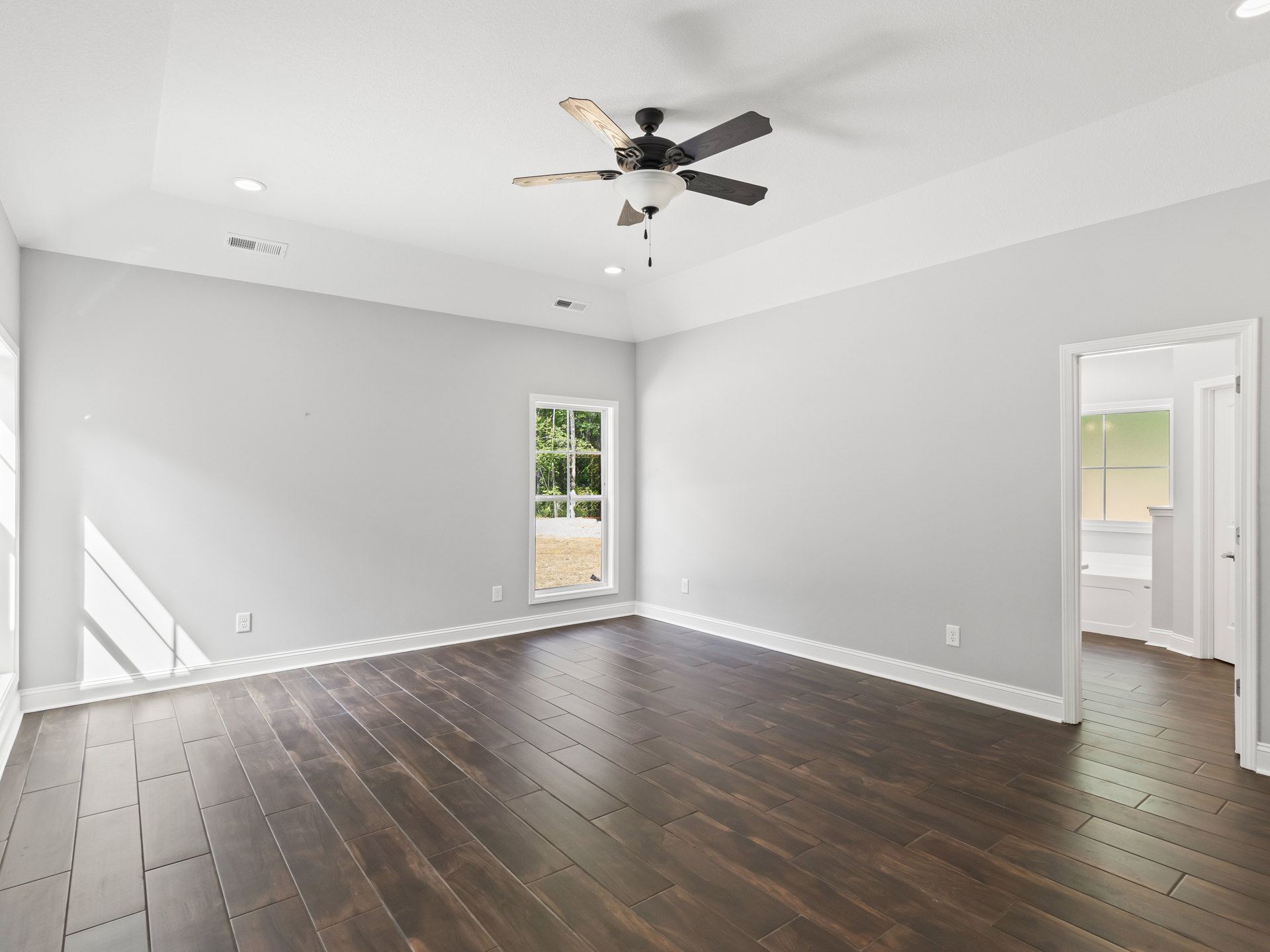 Ceiling fan with light fixture, hardwood floors, white walls, large window overlooking trees, natural light casting shadows