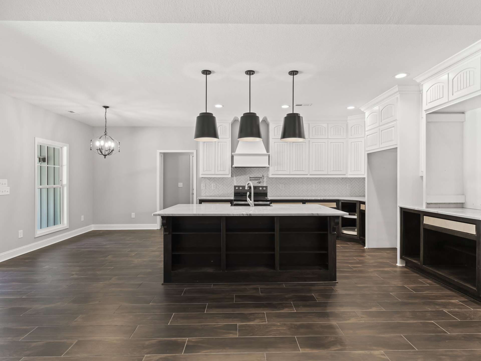 Spacious kitchen featuring a large marble island with open shelves, white-framed window, black lamp shade, white ceiling, modern faucet near stove, and chandelier overhead.