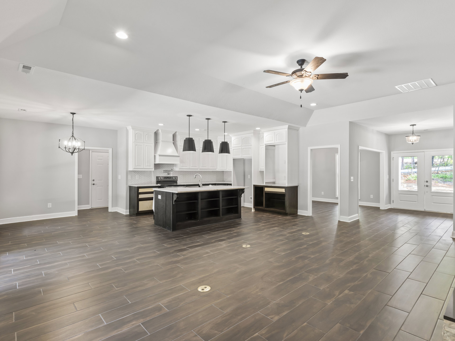 Spacious room featuring wood flooring, ceiling fan with light fixture, kitchen island with open shelves, and chandelier with clear glass shade