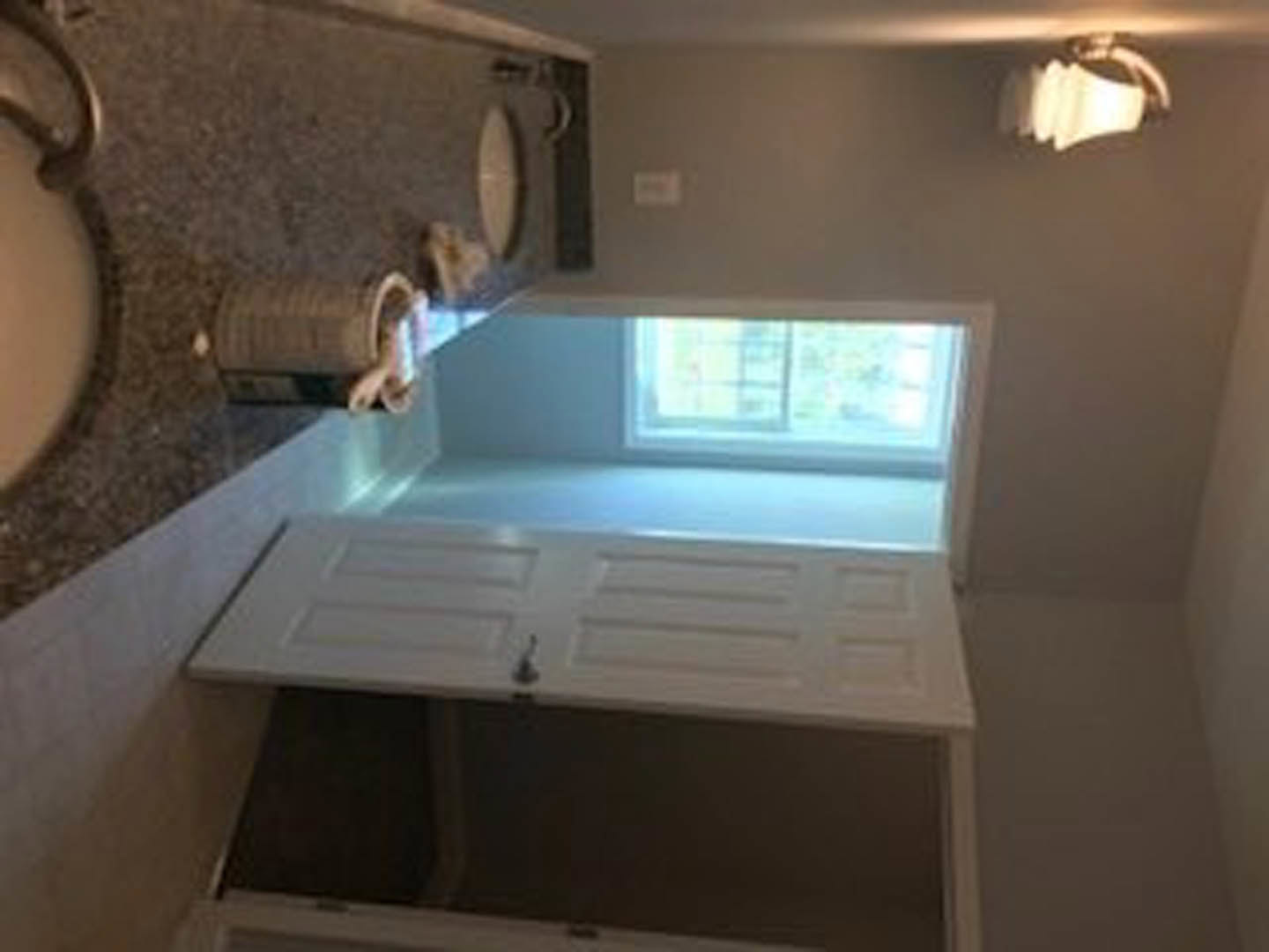 White paneled door with glass window set in a light-colored wall, adjacent to modern kitchen cabinetry and countertop with stainless steel sink and faucet.