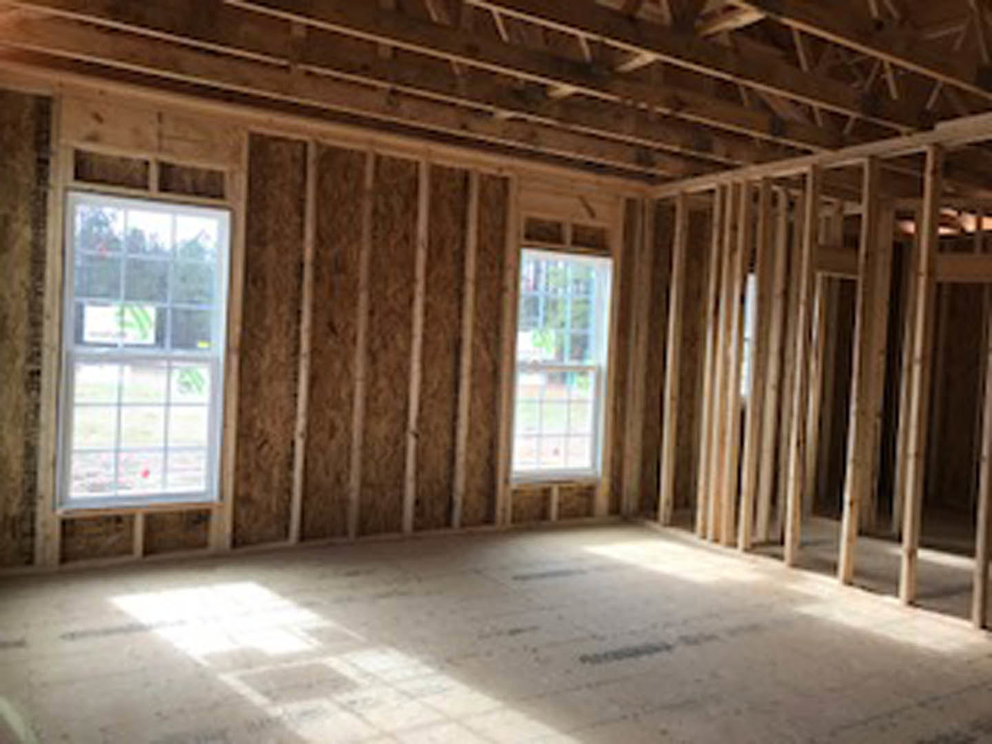 Bright room featuring exposed wood ceiling beams, multiple-paned windows, hardwood flooring, and natural light casting shadows across the floor.
