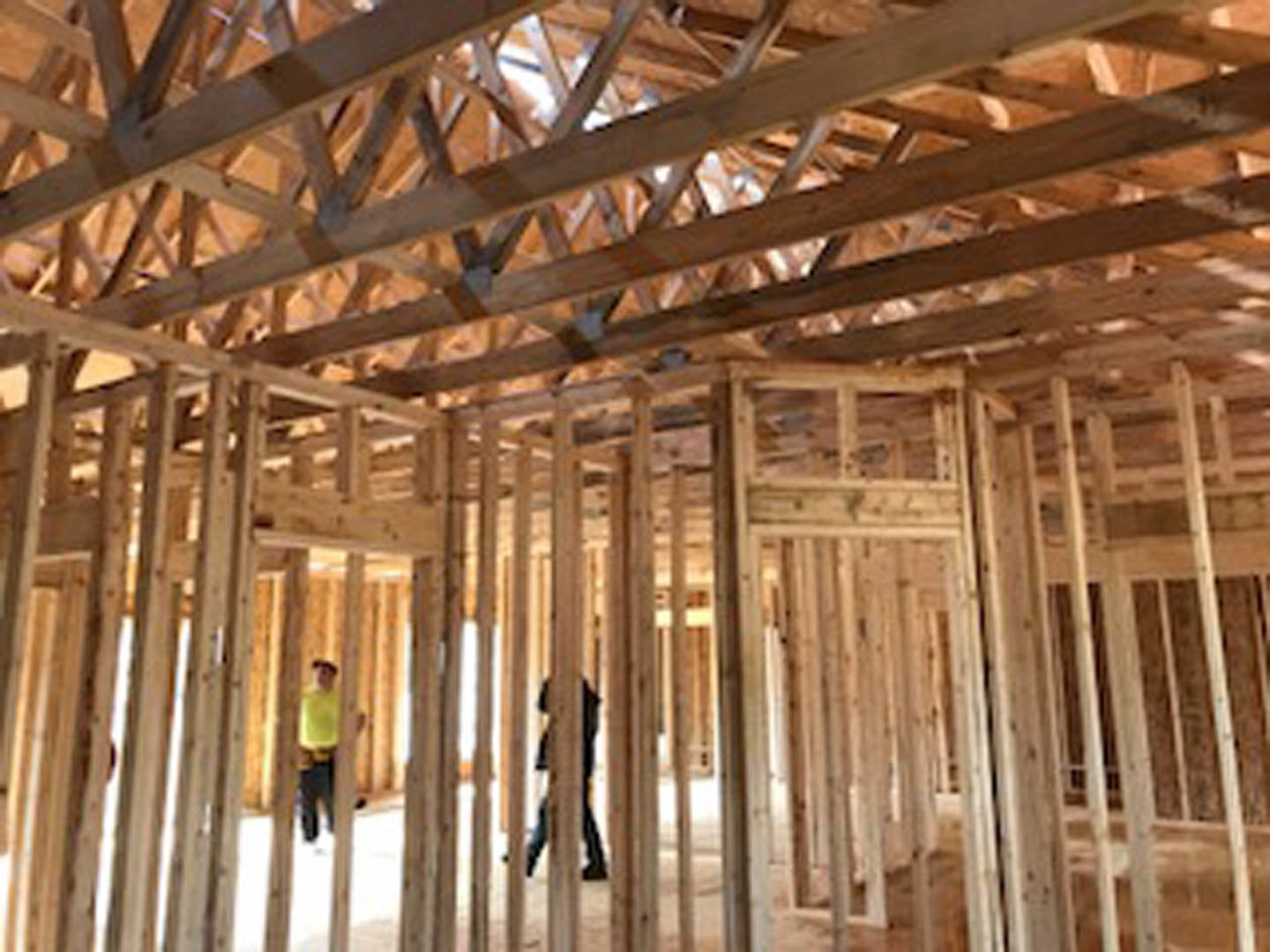 Man walking through unfinished wood-framed interior with exposed beams and ceiling during daylight construction.