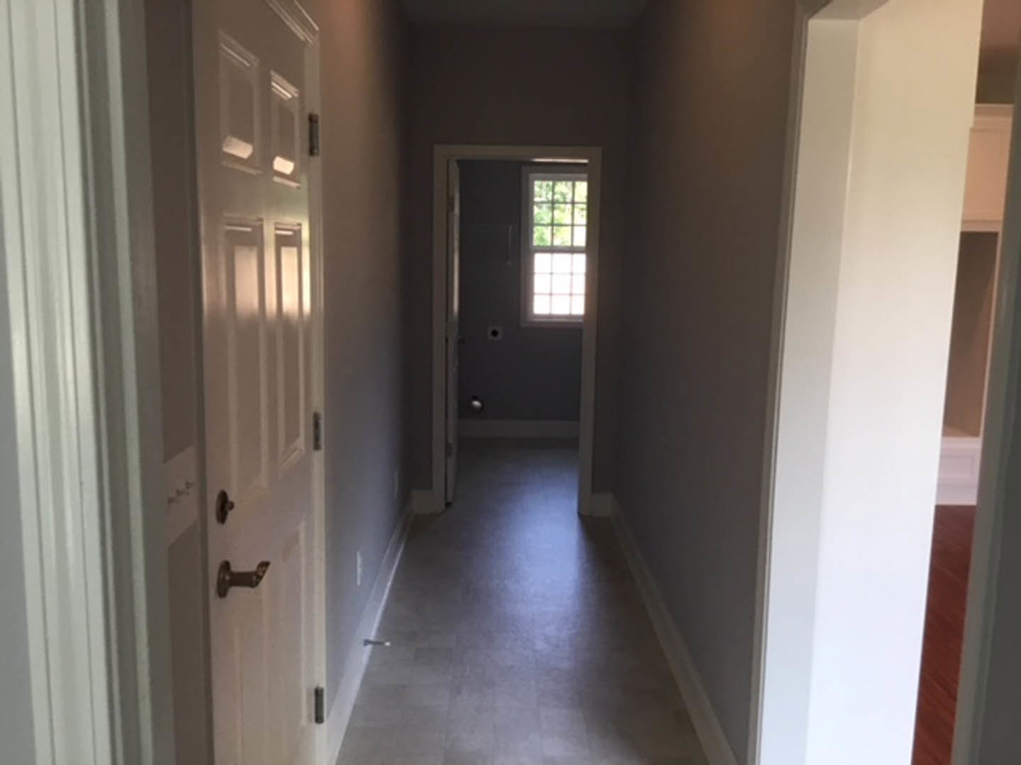 White hallway with paneled door, multi-pane window, light wood flooring, and sunlight streaming across plaster walls