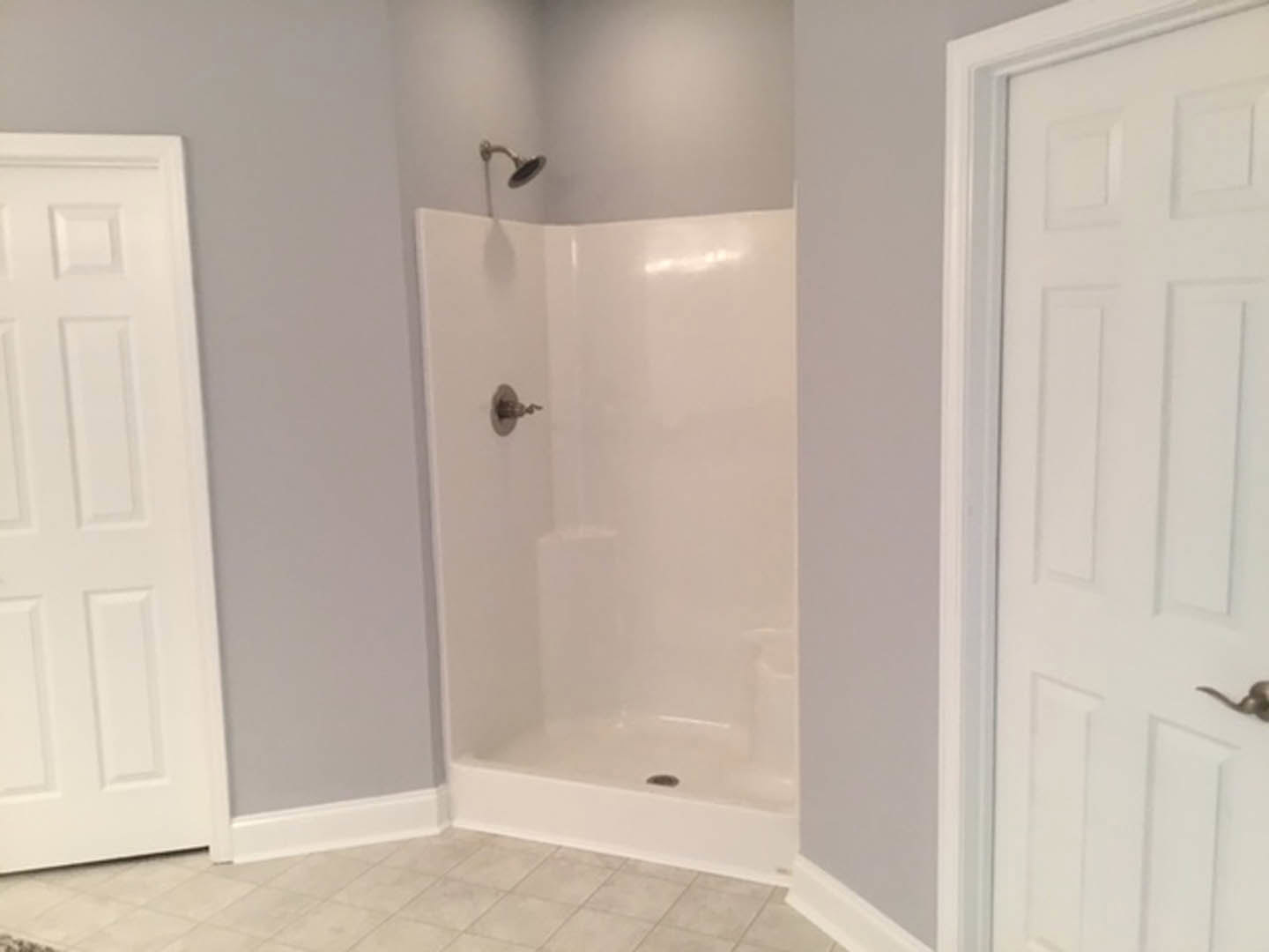 White tile shower with chrome faucet, square-framed white door, and matching white trim in a modern bathroom.