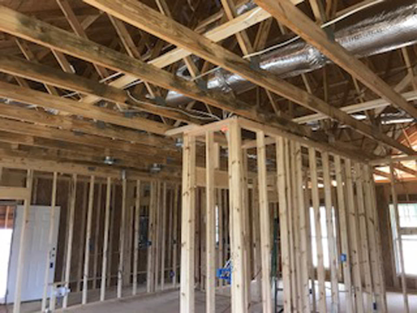 Exposed wood framing and beams with visible metal pipes, unfinished ceiling, and a white door illuminated by natural light in a house under construction