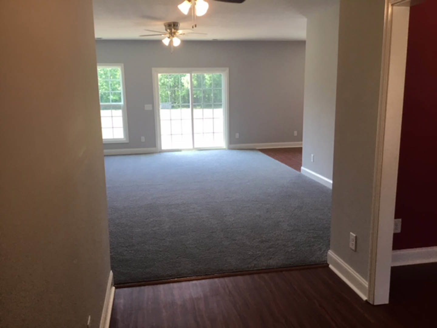 White paneled door with glass panes, large windows, beige carpet flooring, wood laminate floor transition, ceiling fan with lights, white plaster walls