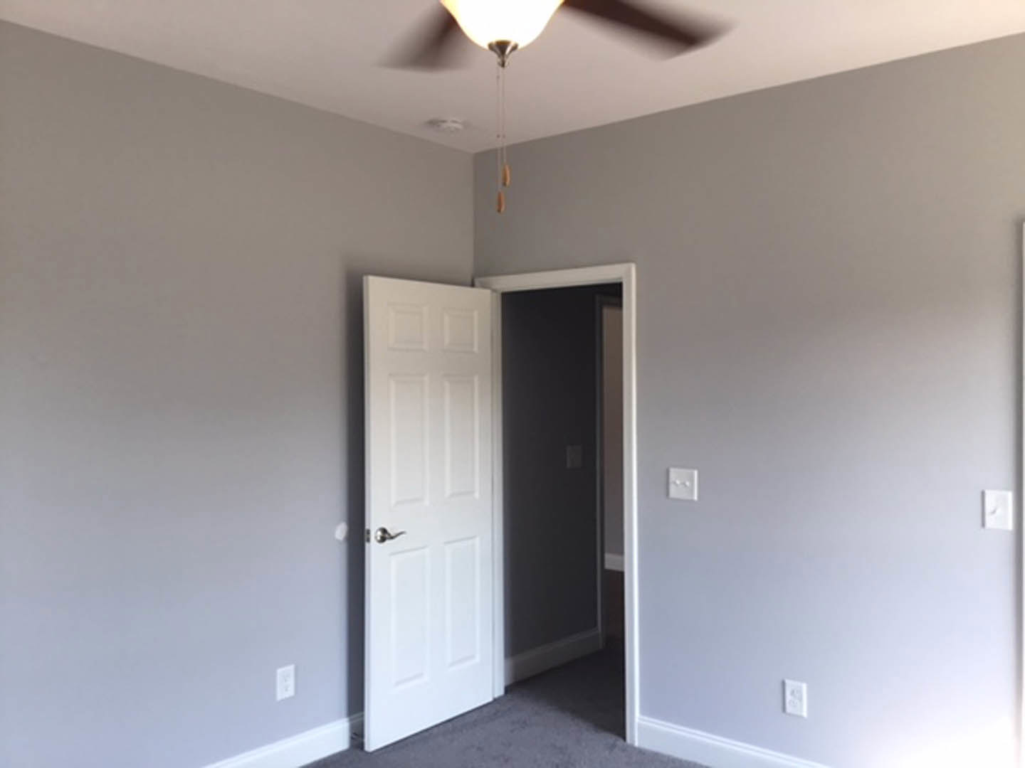 White paneled door with brushed metal handle, white wall featuring a light switch, ceiling fan with light fixture, neutral painted walls, and light-colored flooring
