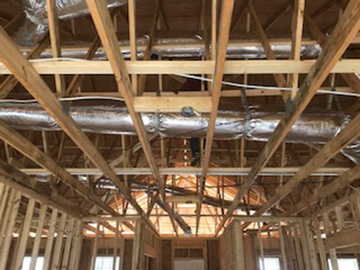 Exposed wood framing and ceiling beams with visible heater unit and insulated pipes in unfinished interior space