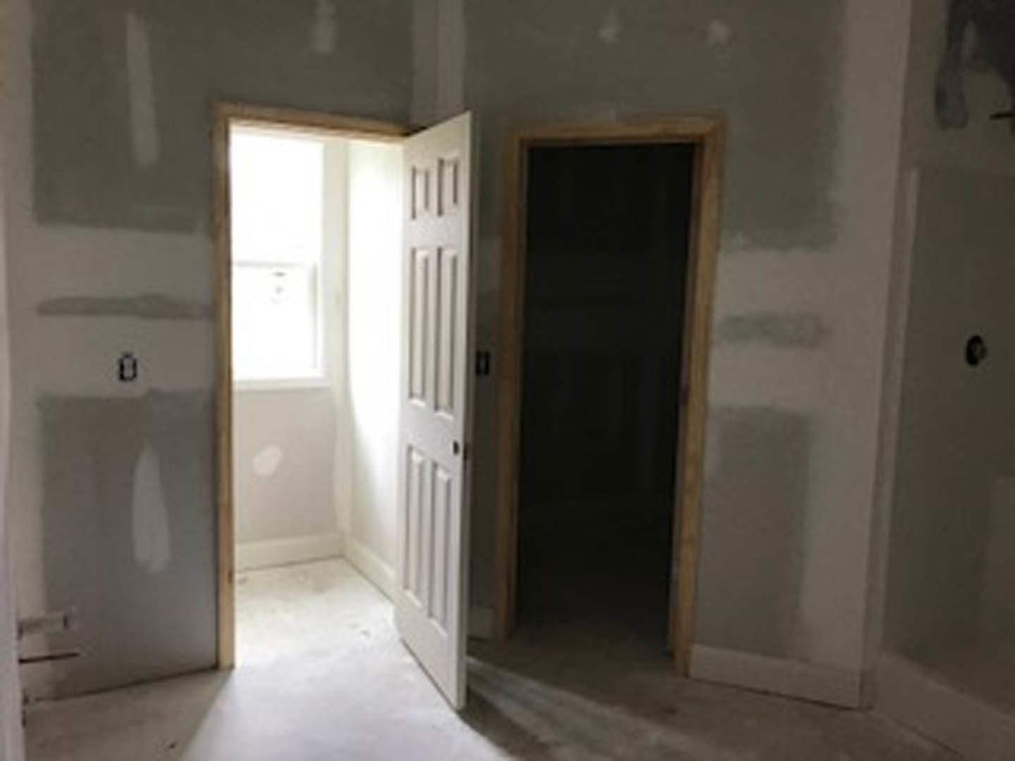 Open white door with black handle leading into a room with light-colored walls, large window, and smooth flooring.