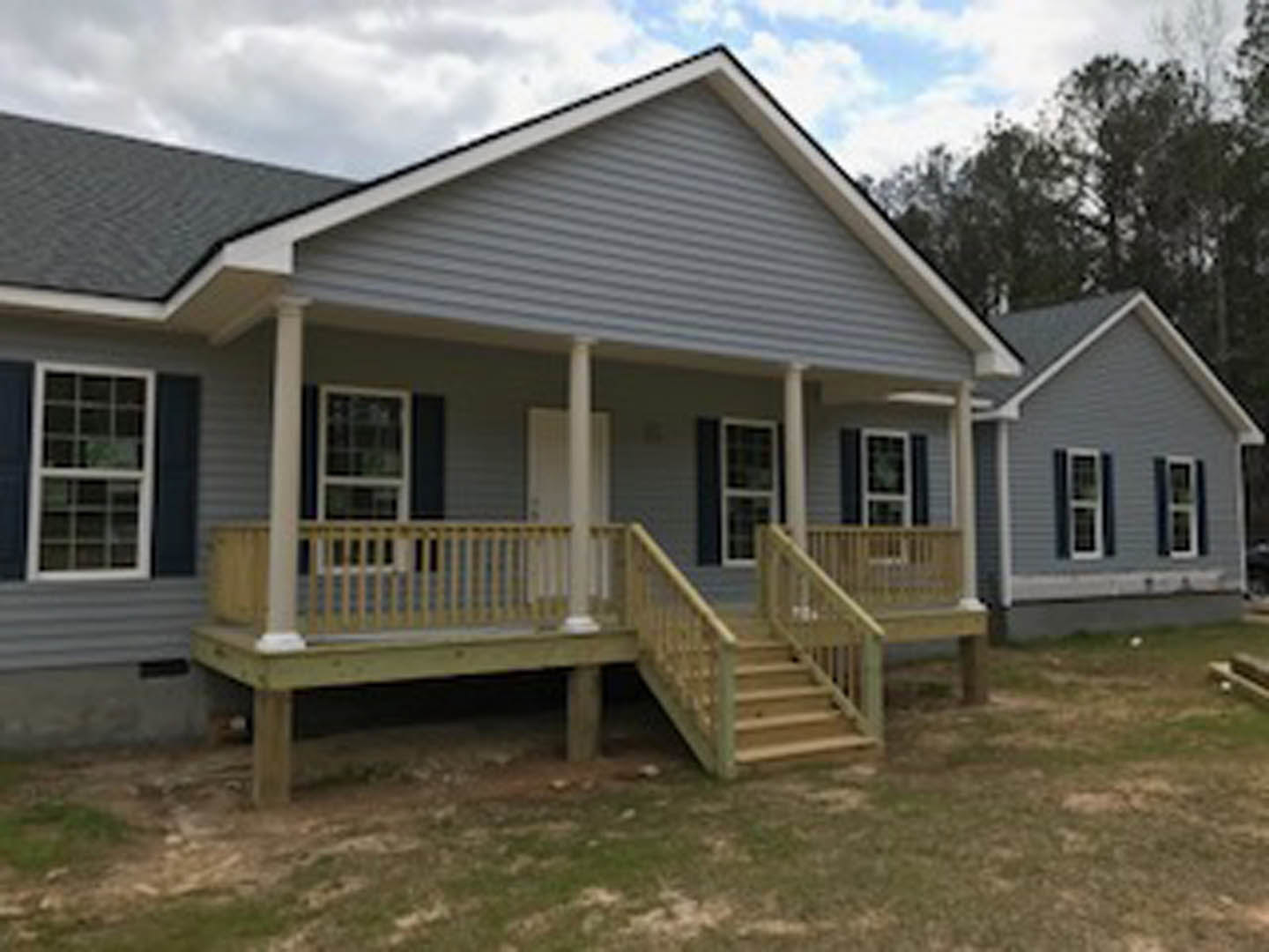 Two-story home with light siding, wooden porch and stairs, white railing, multiple windows with white frames and square panes, outdoor entry area
