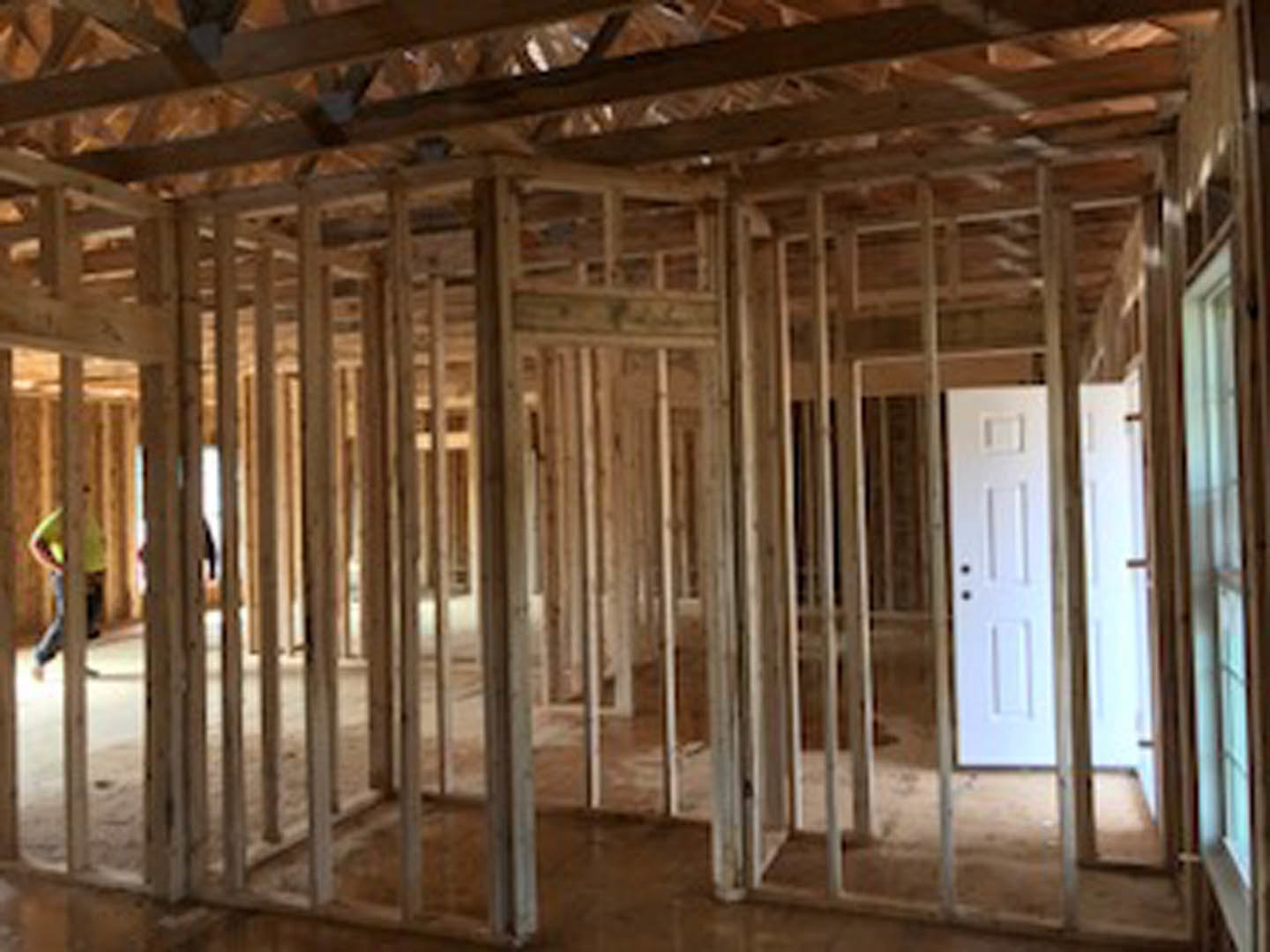 Open room with exposed wooden ceiling beams, light-colored flooring, and a white door set in a finished wall.