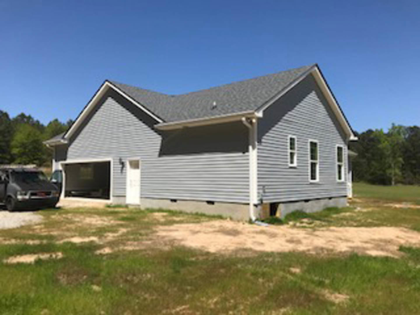Two-story house with attached garage, white front door, gable roof, dirt patch and grass in front, parked car partially visible, blue sky overhead