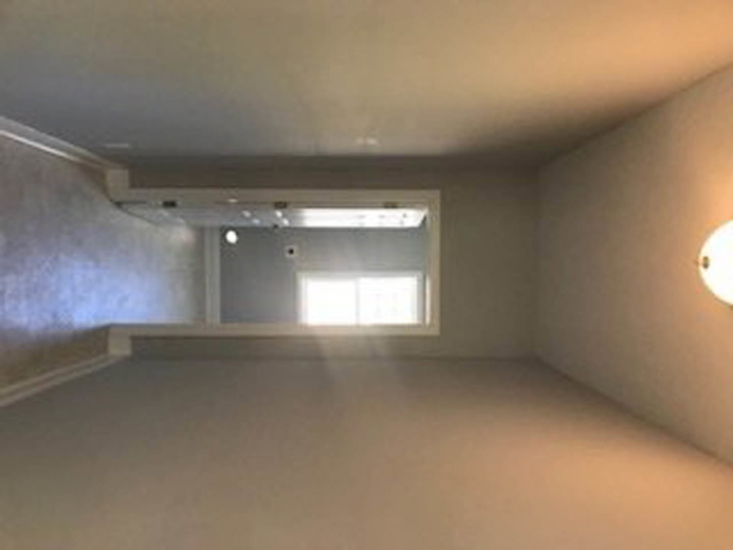 Sunlit room with plaster walls, wood flooring, large window, and white door; natural light casts soft shadows across interior.