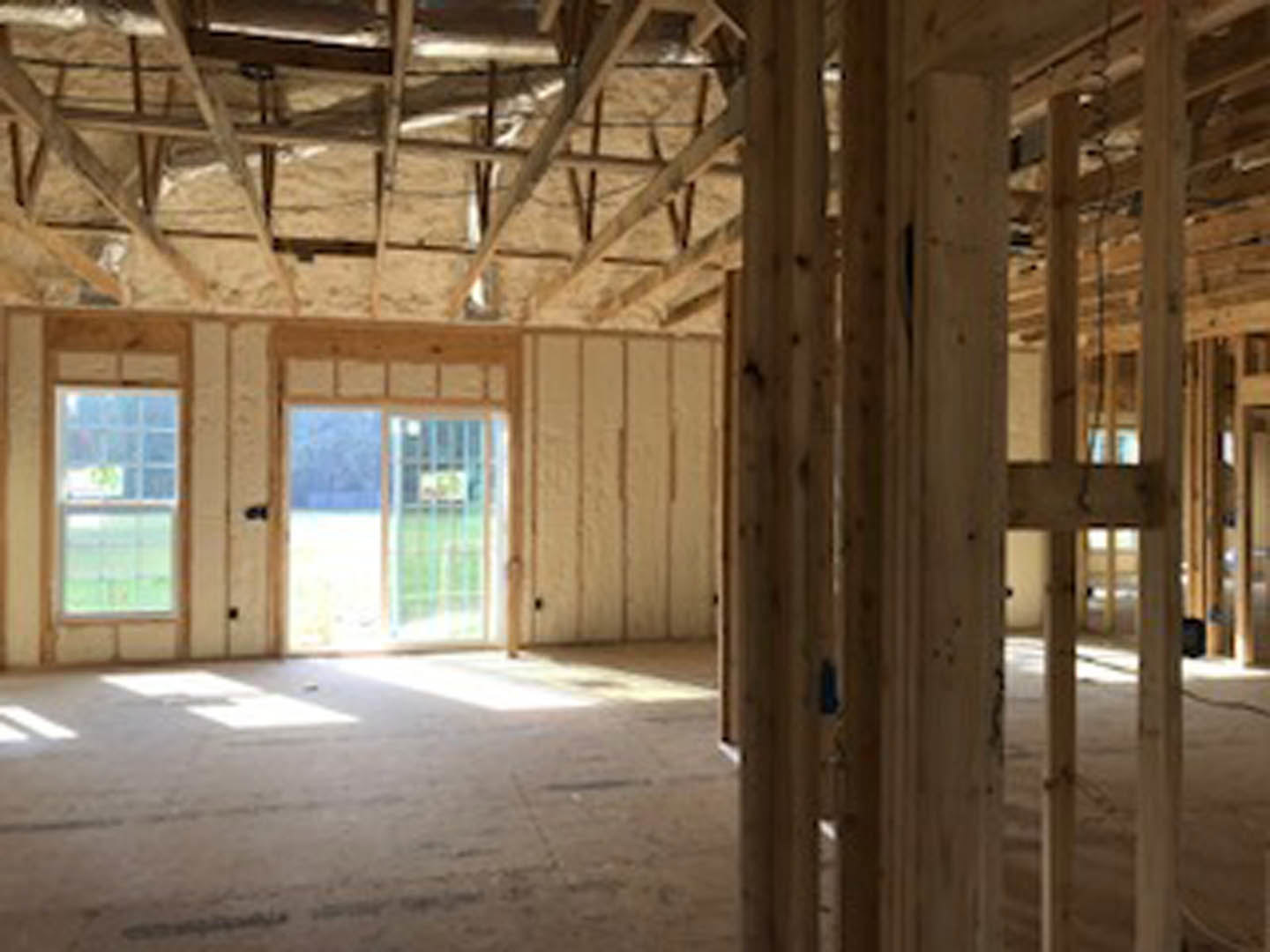 Room with exposed wood beams, white walls, large window overlooking grassy field, and a wooden door