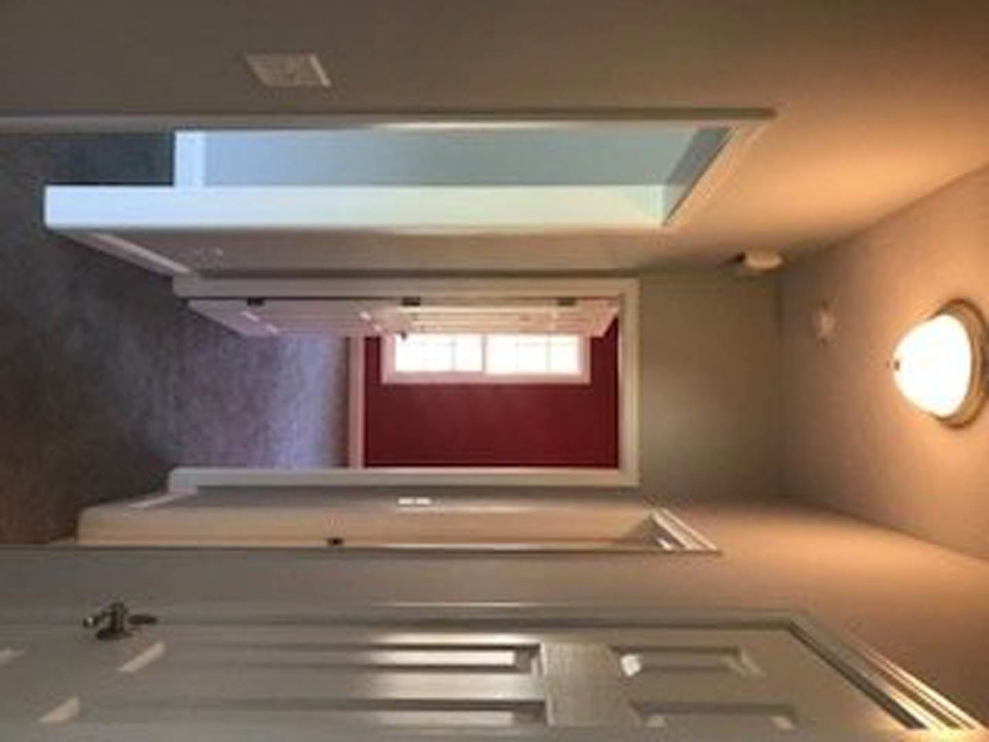 Hallway with bold red wall, white paneled doors, smooth plaster ceiling, and ceiling light fixture