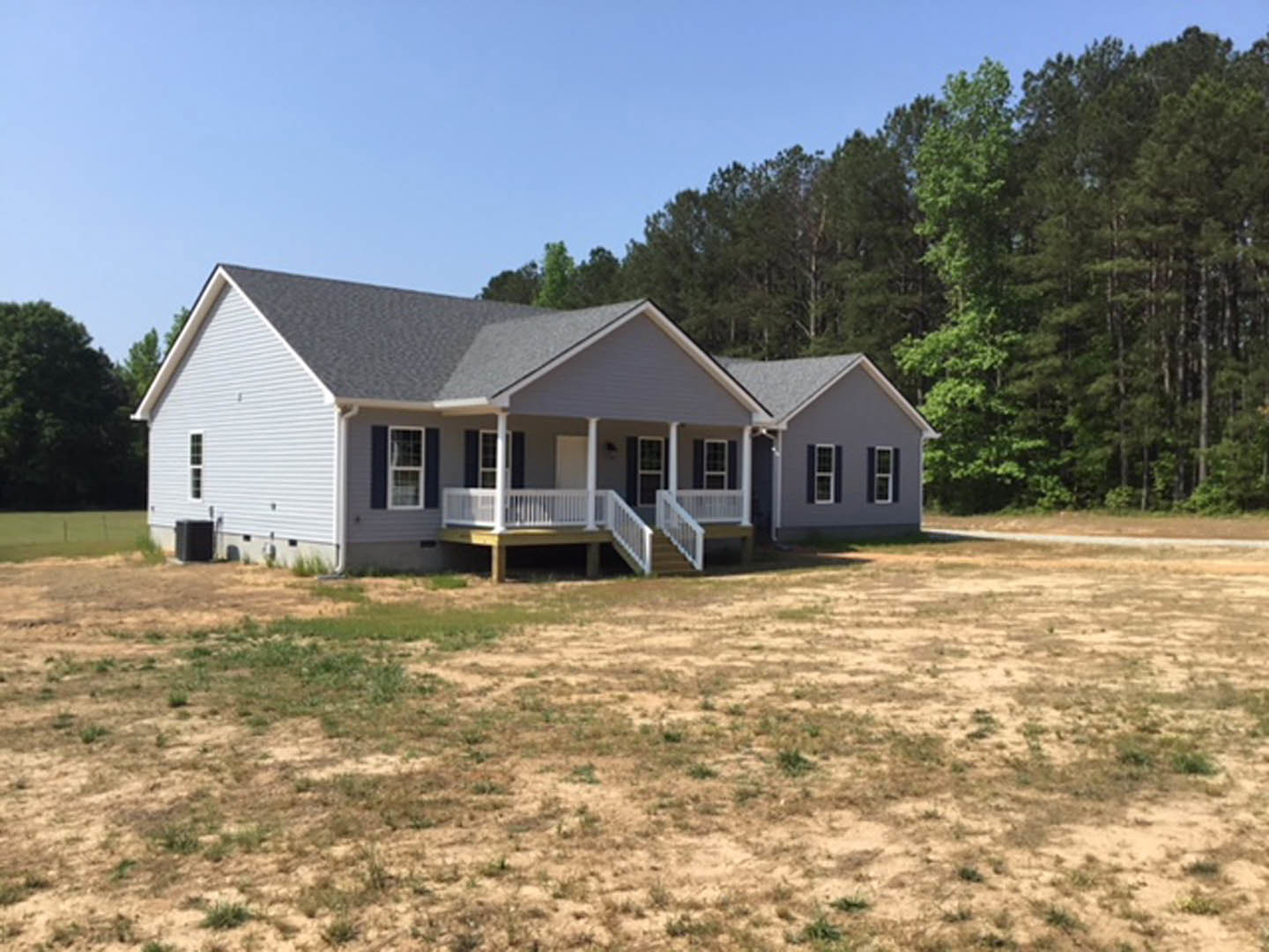 Two-story cottage-style home with white porch railing, wide front steps, expansive grassy yard, mature trees, and large windows with white frames
