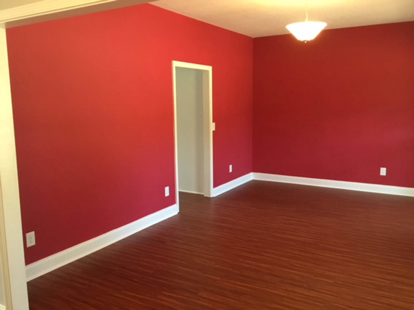 Red walls with white trim, wood laminate flooring, white door, ceiling-mounted light fixture