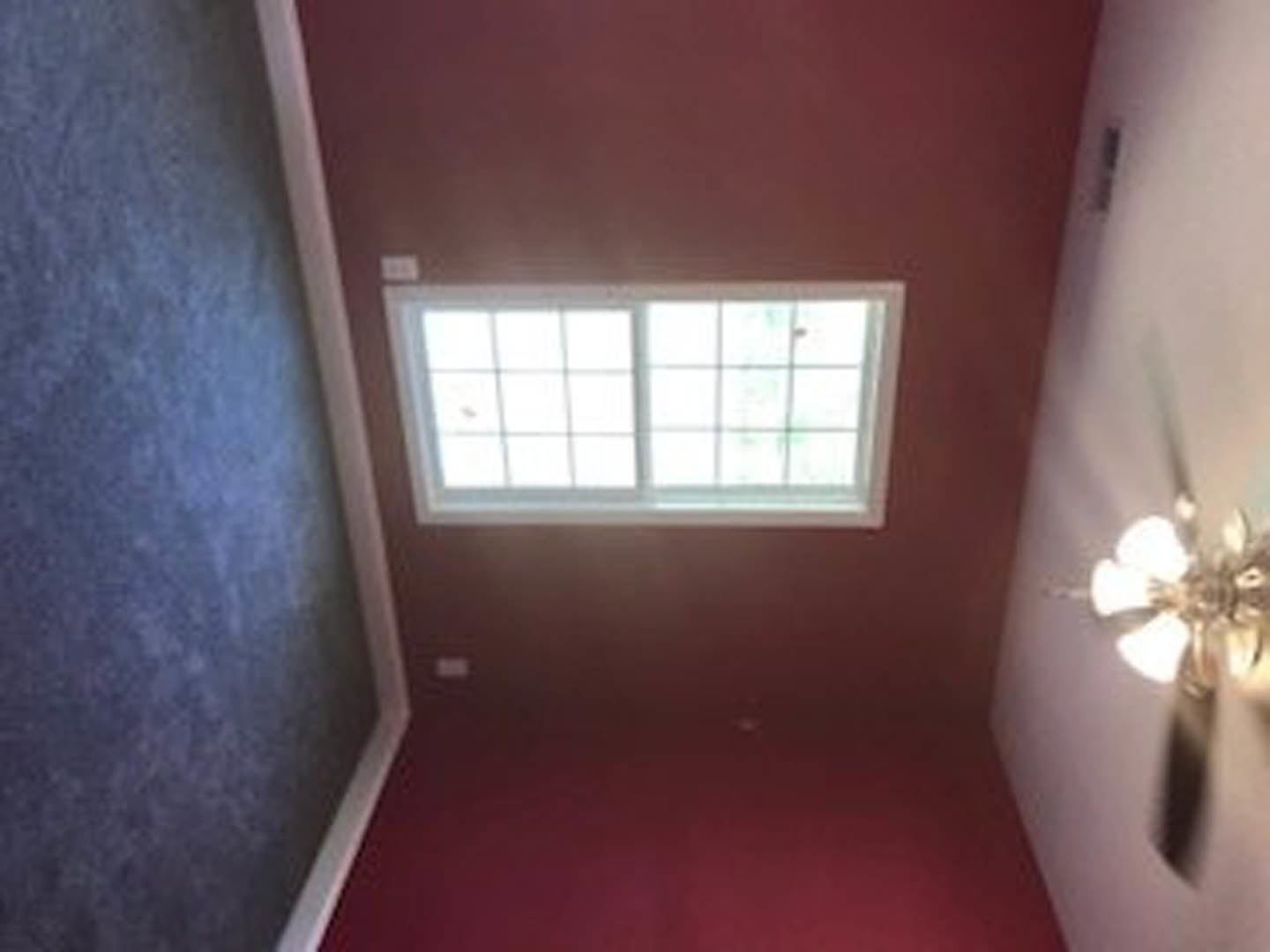 Sunlit room with white plaster walls, large window framed in brown trim, red accent wall, ceiling fan, and decorative molding.