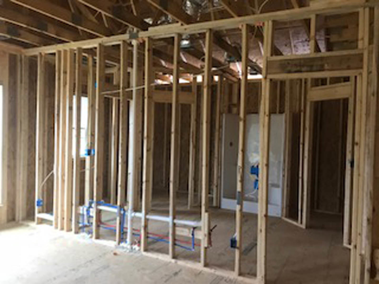 Room under construction with exposed wood framing, ceiling beams, and partially installed insulation