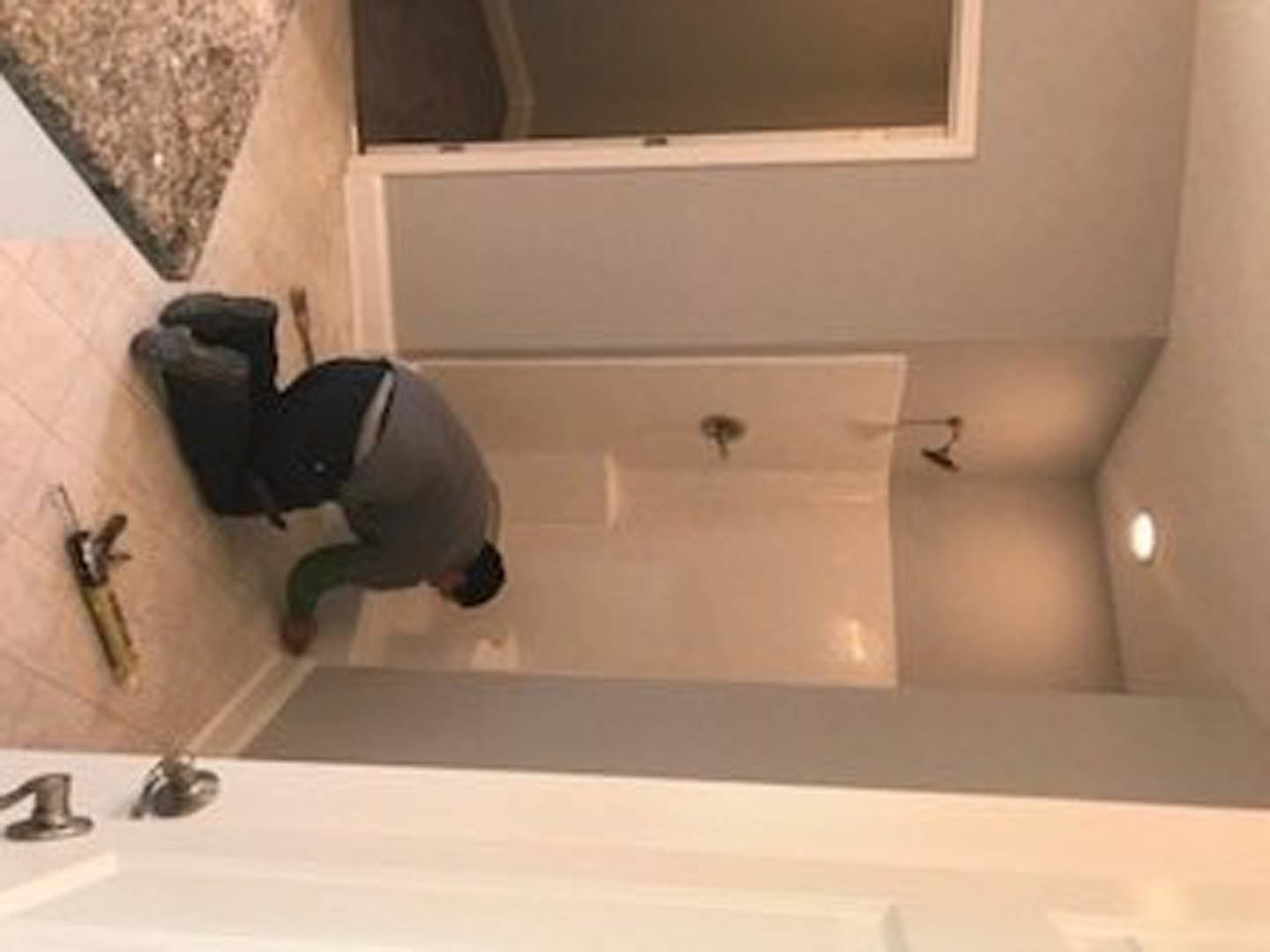 Man standing in modern bathroom with white tile walls, freestanding tub, wall-mounted sink, large mirror, and chrome fixtures