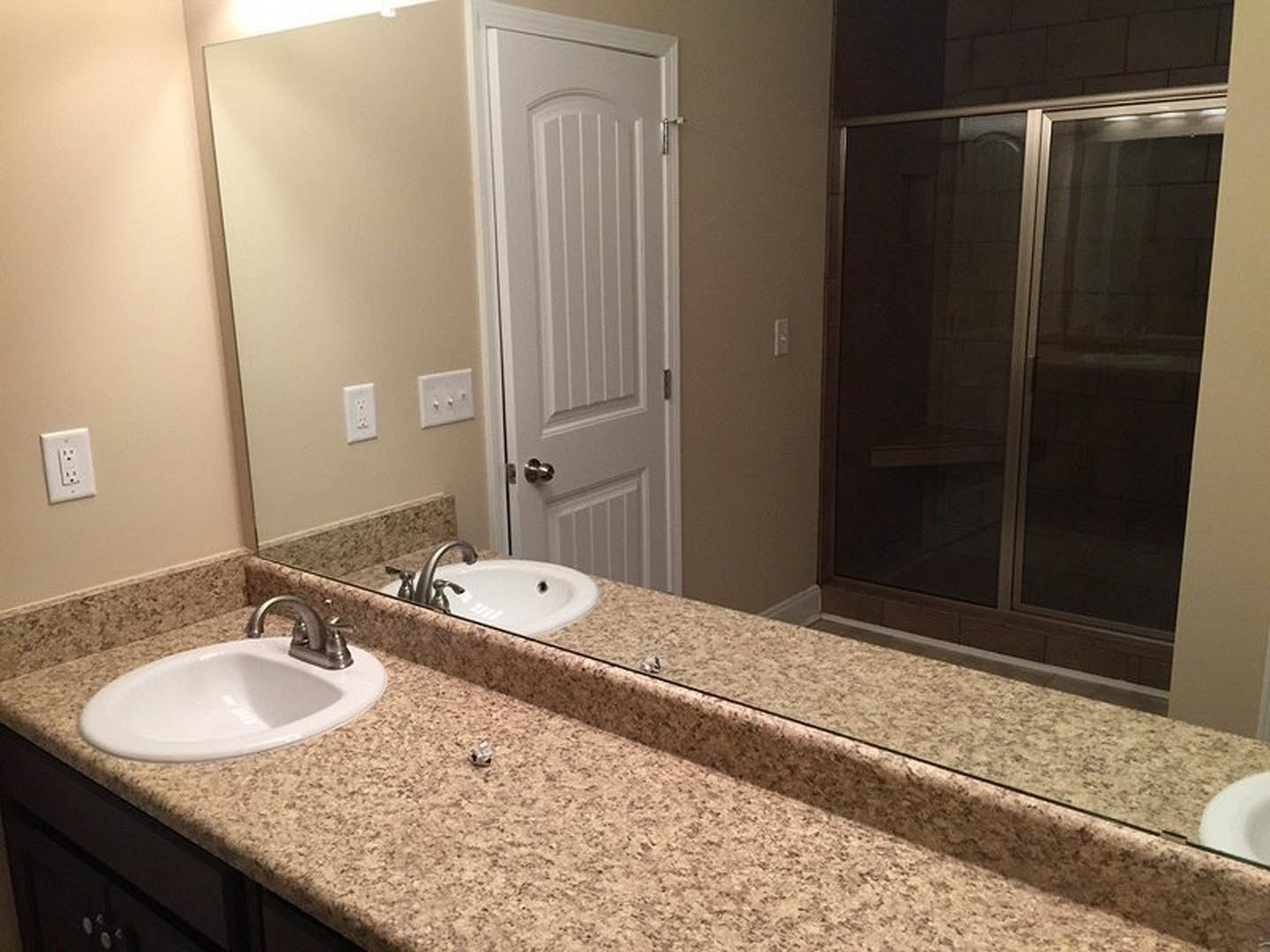 Bathroom with a large wall mirror above a white sink and chrome faucet, glass shower enclosure, white door, and tiled walls with visible electrical outlet