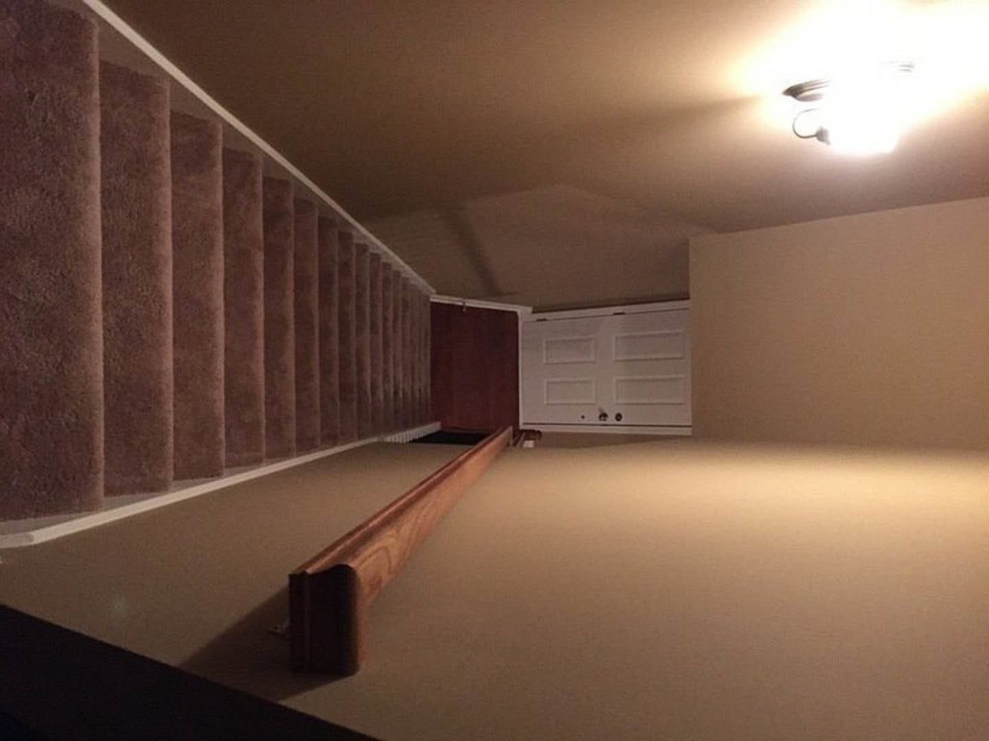 Carpeted staircase with white risers, white cabinet door at landing, wooden board resting on carpeted floor, black metal handrail, ceiling light fixture with exposed wire, plaster