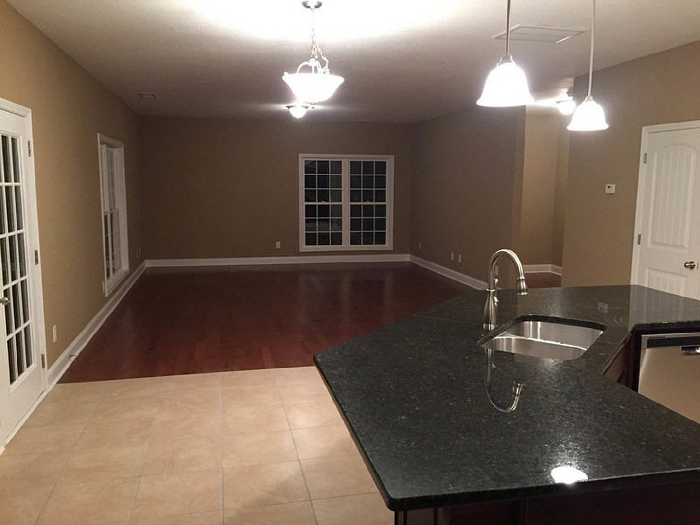 Modern kitchen featuring black stone countertop with built-in silver sink, white tile backsplash, multiple square-paned windows, pendant ceiling lights, and sleek cabinetry.
