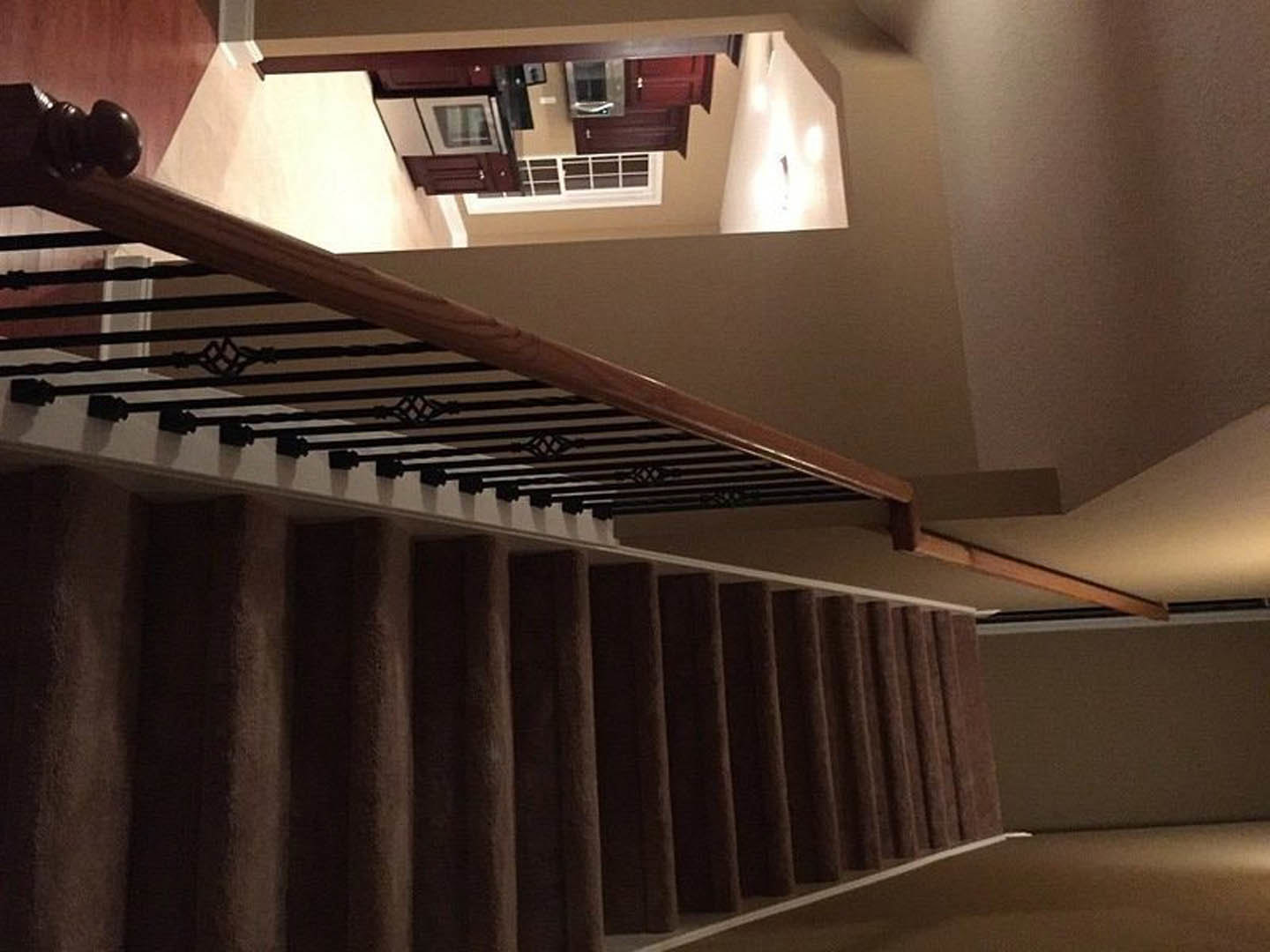 Brown carpeted staircase with black and white striped railing, white-framed window with grid, light-colored walls, and indoor shelving.
