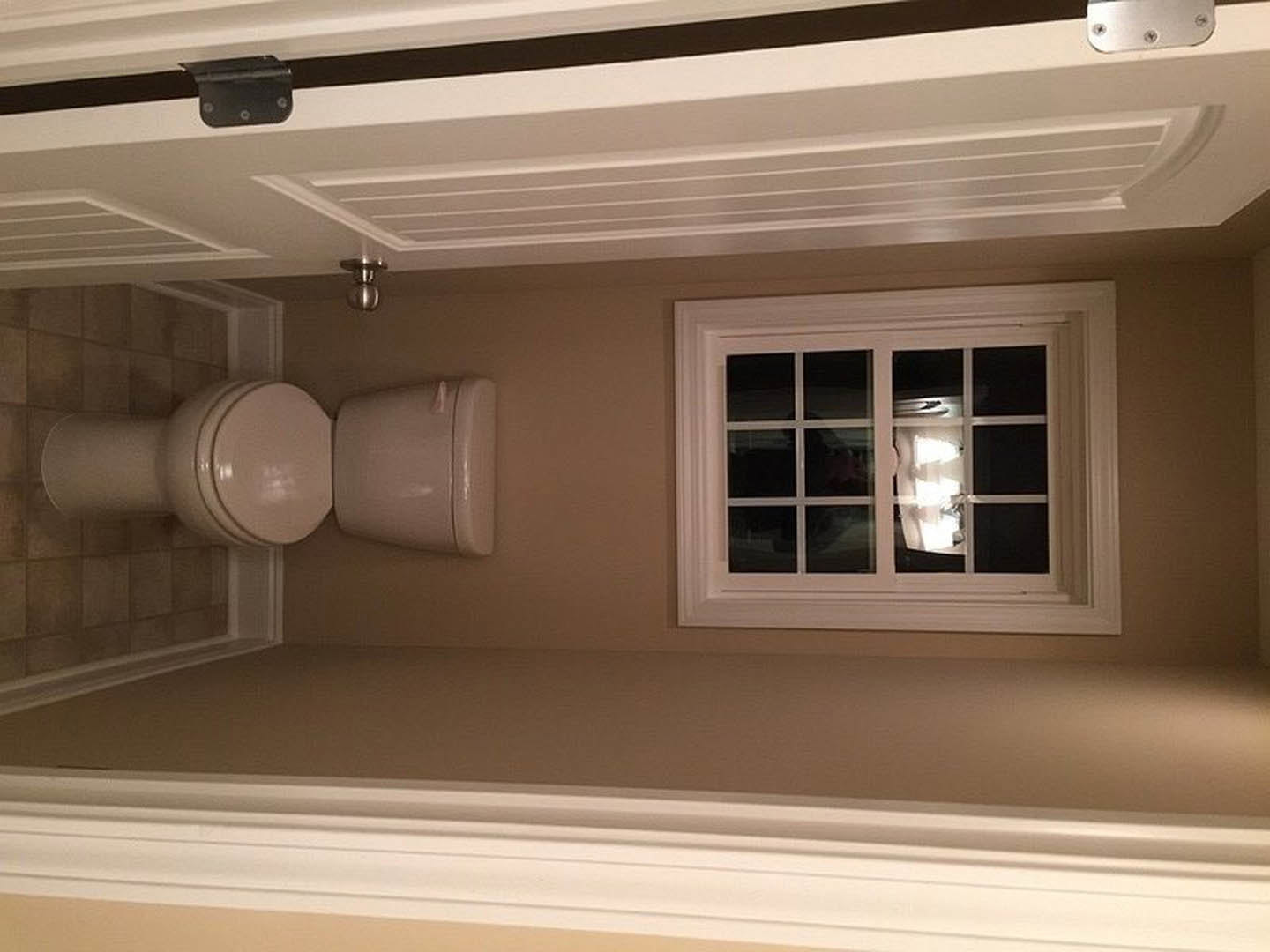White bathroom with a window, toilet with lid up, plaster walls, ceiling molding, and ceiling light fixture reflected in window glass
