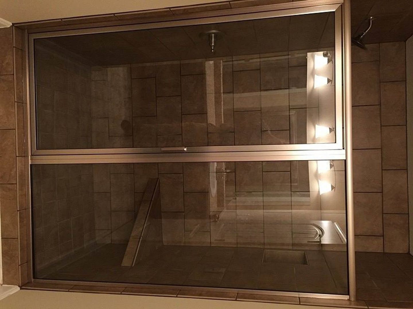 Frameless glass shower enclosure with chrome hardware, white tile walls, built-in lighting, and adjacent bathtub with white trim