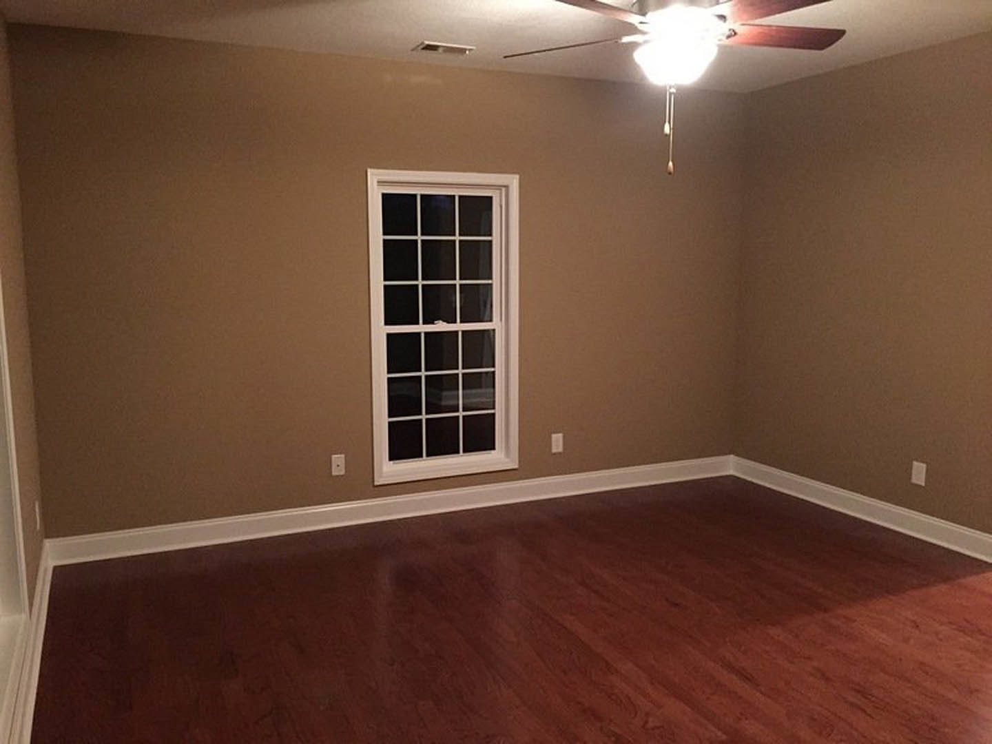 Bedroom with hardwood flooring, white plaster walls, large window, and ceiling fan with light fixture