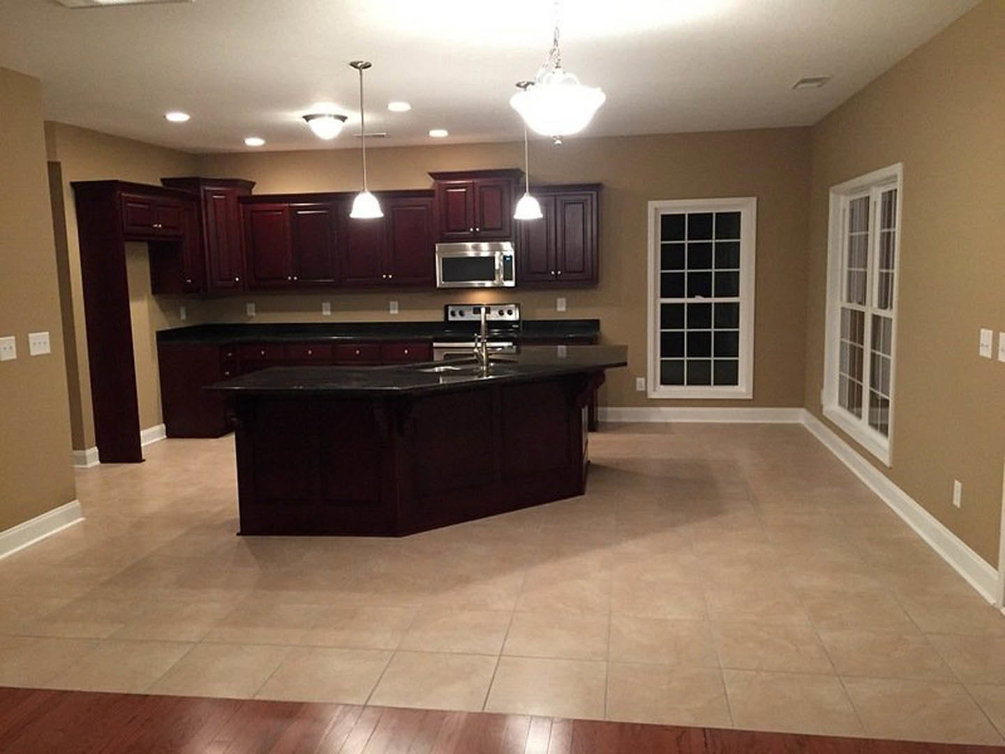 Kitchen featuring dark wood cabinets, large central island with built-in sink, tile and wood flooring, stainless steel microwave, and multiple square-paned windows.
