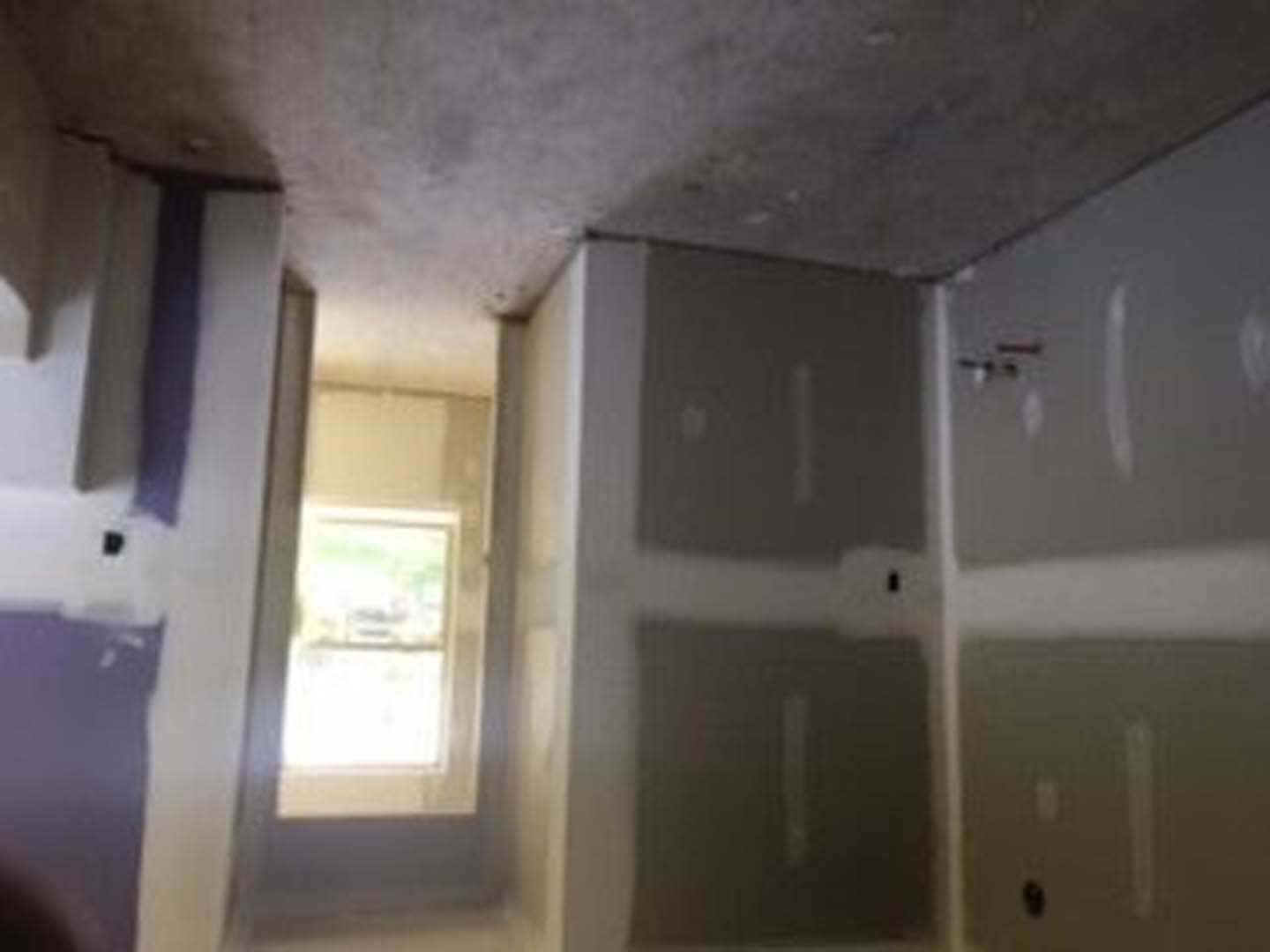 Bathroom with white plaster walls, window with natural light, light-colored floor, and a door partially visible in the foreground