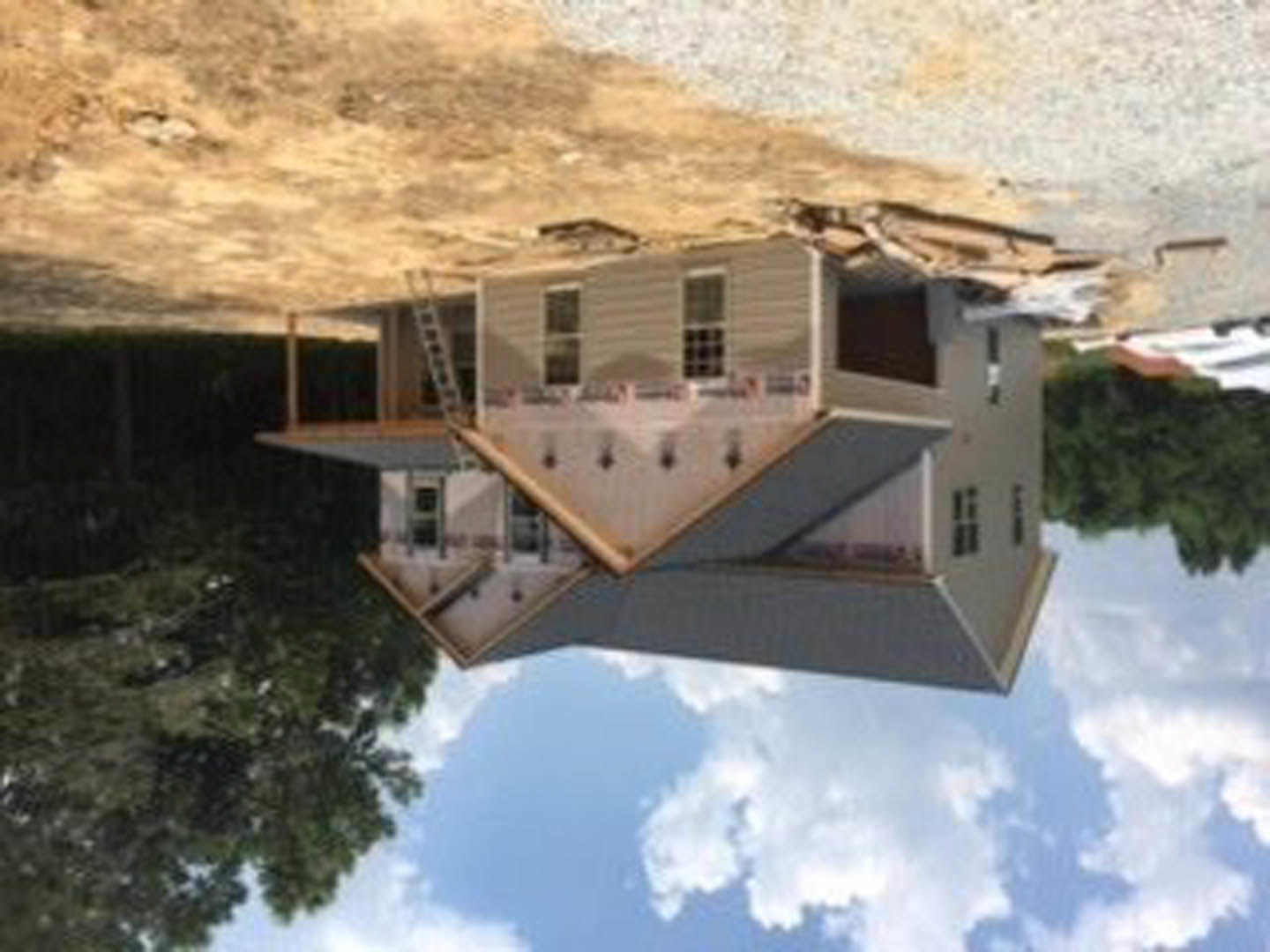 Modern home with partially collapsed roof, large windows, surrounded by trees and hills under cloudy sky