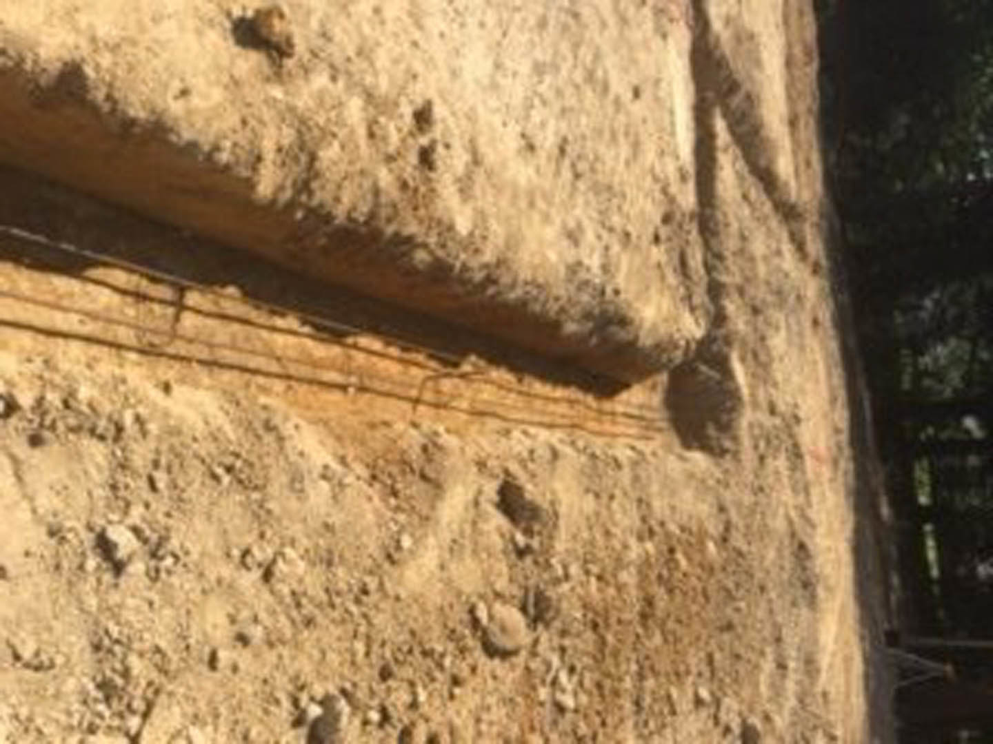 Close-up of textured rock wall with varied stone shapes and earthy tones, exterior brick building in background, outdoor ground visible