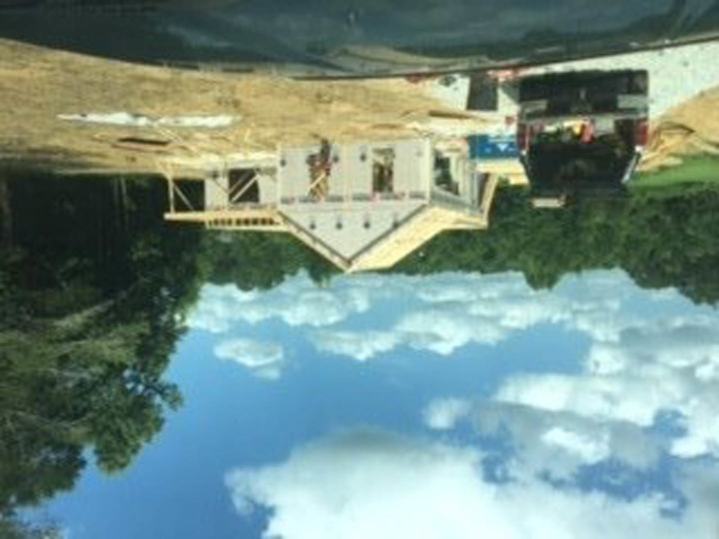 Wood-framed custom home under construction, surrounded by trees, cloudy sky overhead