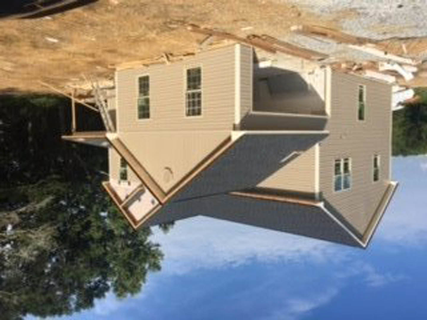 Partially built house framed in wood, surrounded by trees under clear blue sky, with several window openings visible
