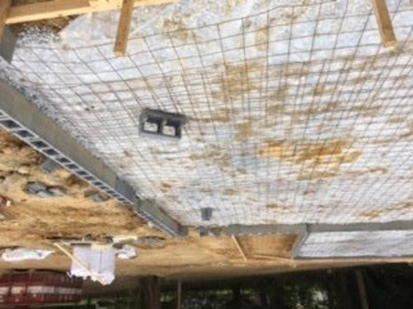 Metal frame with horizontal metal bars set against a wall, wooden furniture leg resting on tile floor, blurry dog in background.