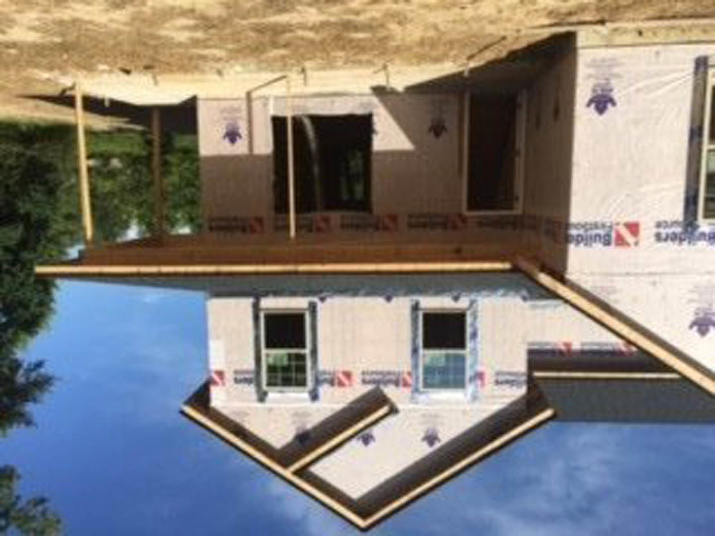 Framed house under construction with exposed wooden beams, unfinished walls, and clear blue sky in background