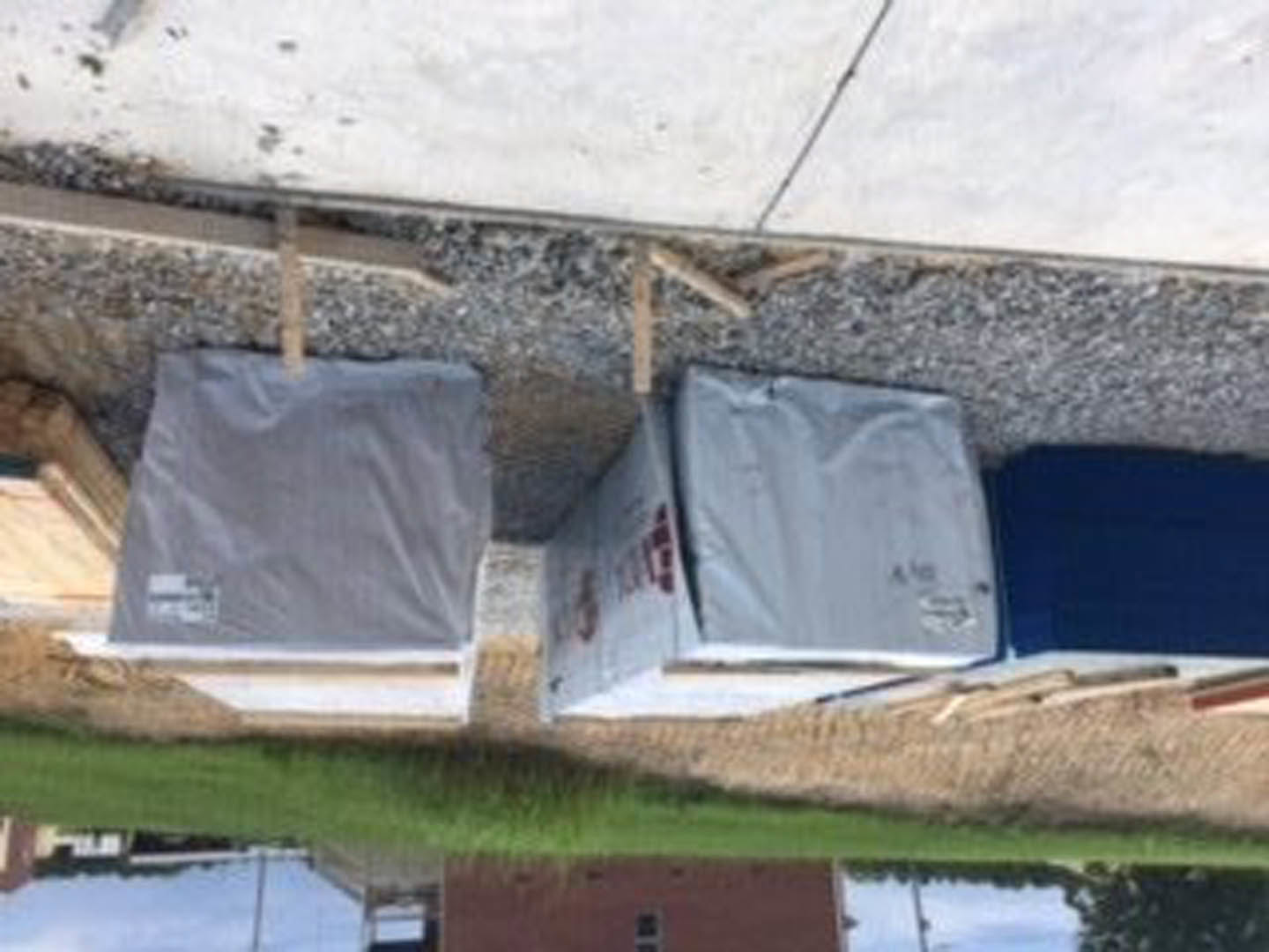 Two box-shaped structures on a gravel path with grass nearby, featuring a blue rectangular object with a white border and a white square object with a label.