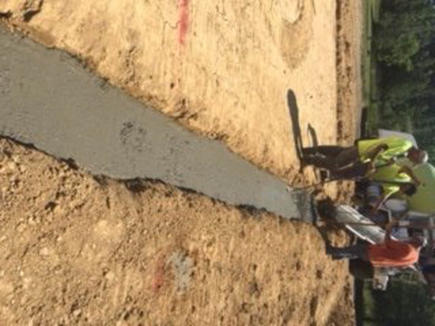 Workers assembling wood framing and pushing a wheelbarrow across soil at a custom home construction site