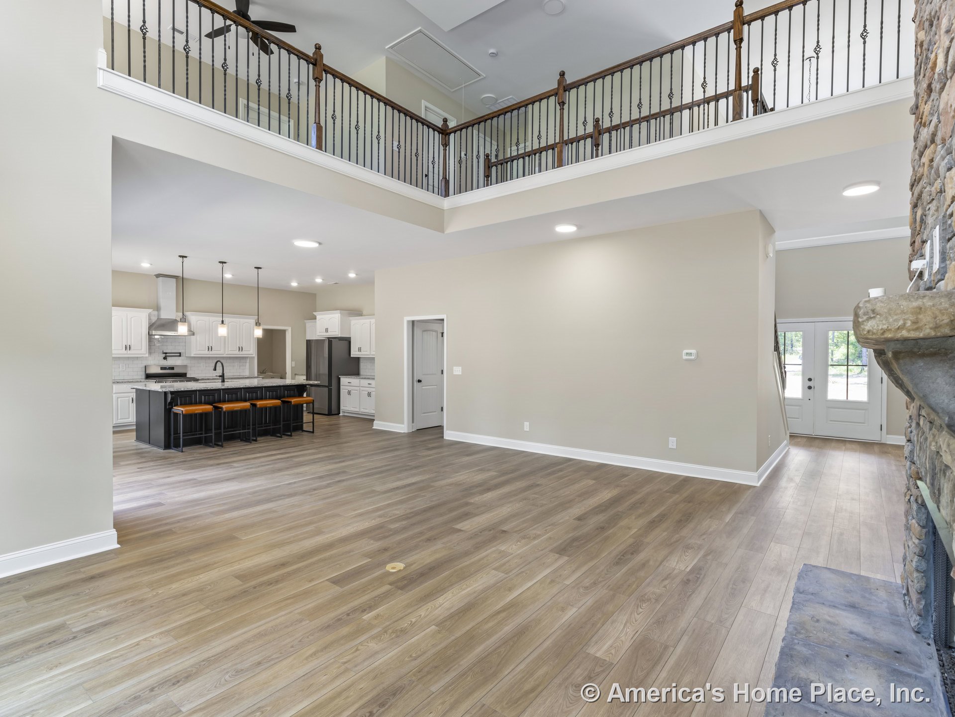Open-concept living area with stone fireplace and mantel, wood plank flooring, white kitchen cabinetry, black kitchen island featuring built-in seating, pendant lights above