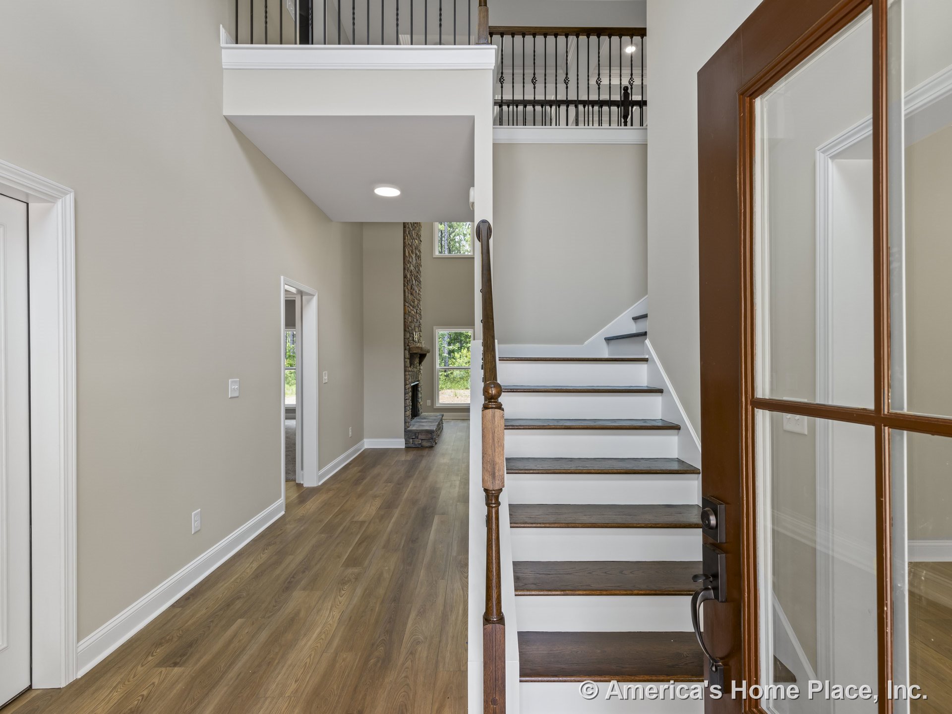 Wood entry door with glass panels opens to foyer with wood flooring, open staircase featuring dark wood treads, white risers, wood handrail, and iron balusters; view extends to