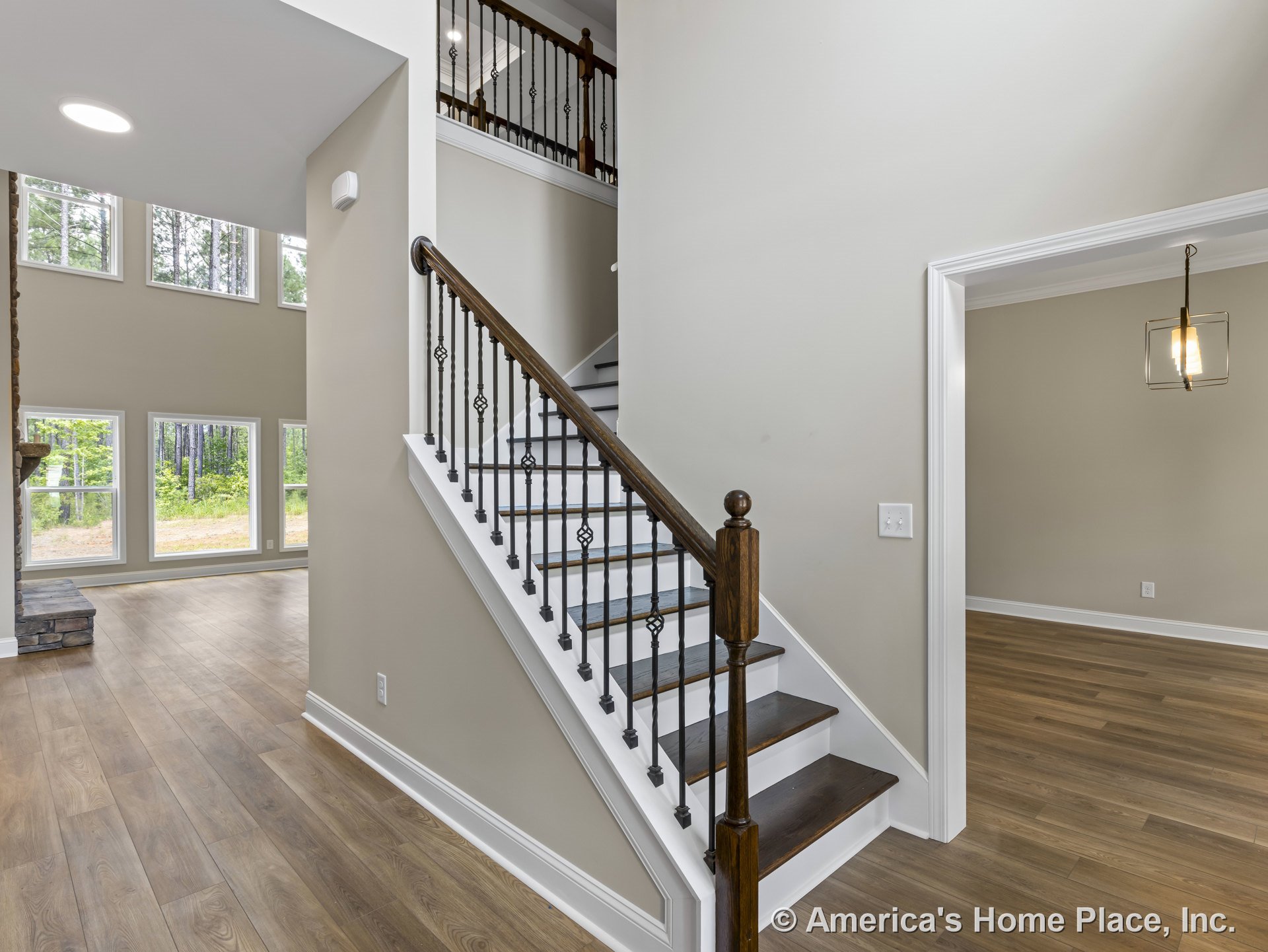 Wood staircase with iron balusters in open foyer featuring tall windows, adjacent dining room with built-in ceiling light fixture, light wood flooring, white trim and baseboards